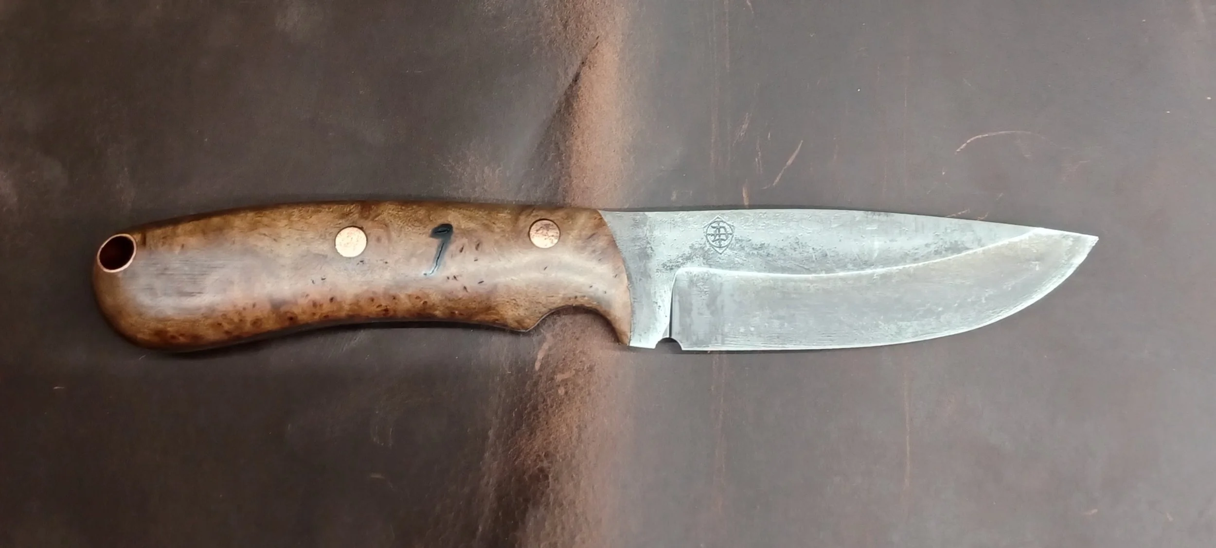 A fixed-blade hunting knife with a wooden handle and a stainless steel blade on a dark surface.