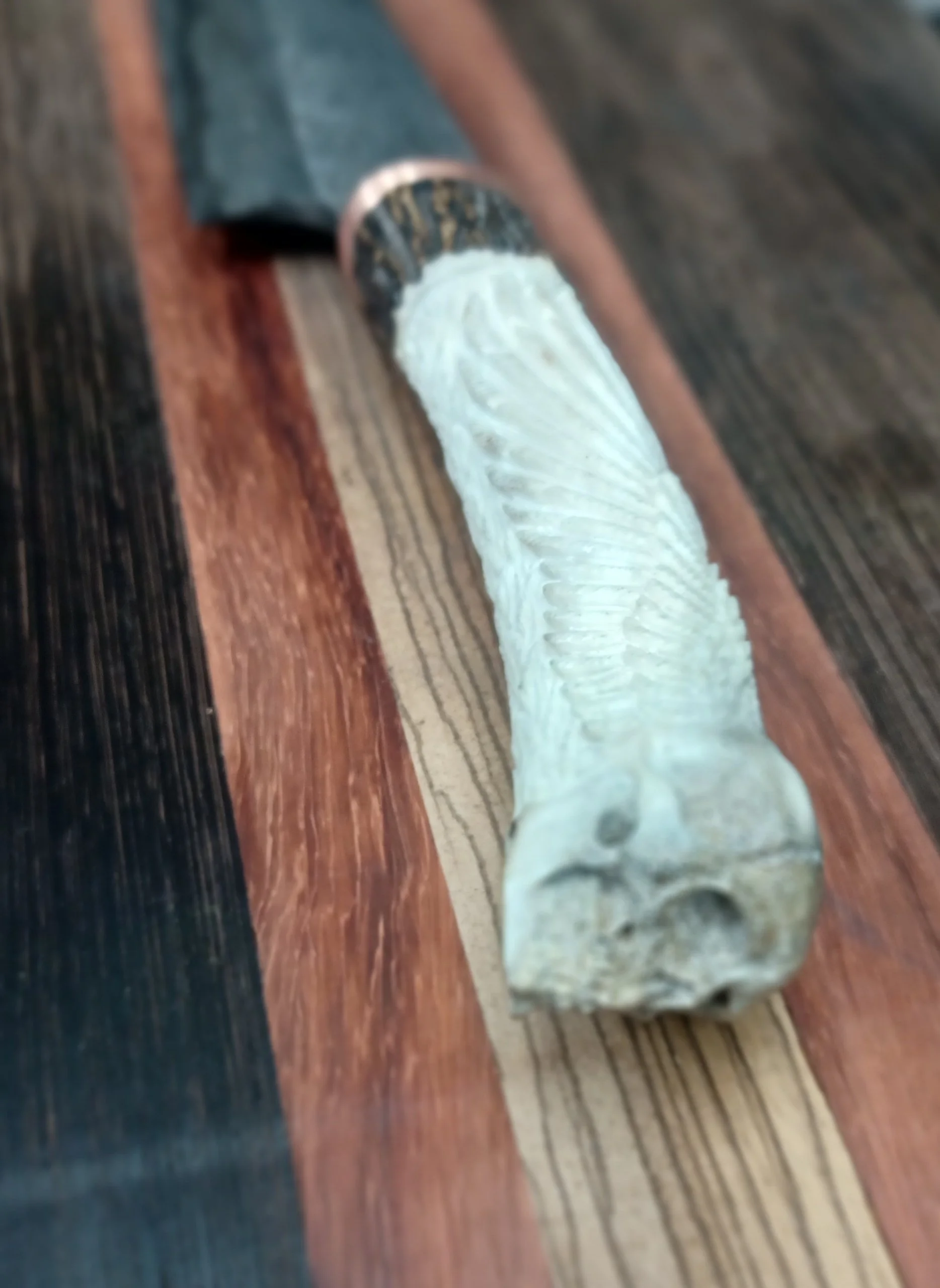 Close-up of a carved knife handle, placed on a wooden surface with dark and light wood strips.