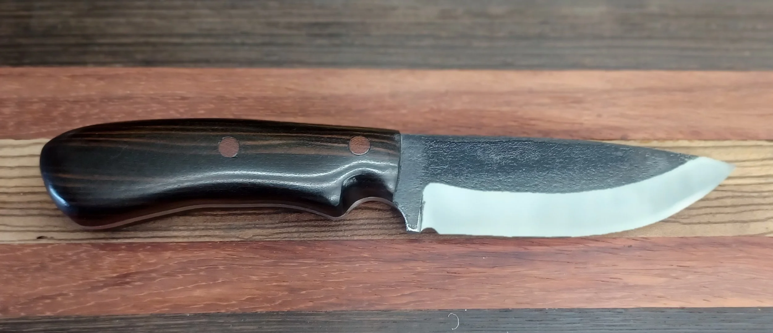 A small knife with a black handle and white blade resting on a wooden surface.