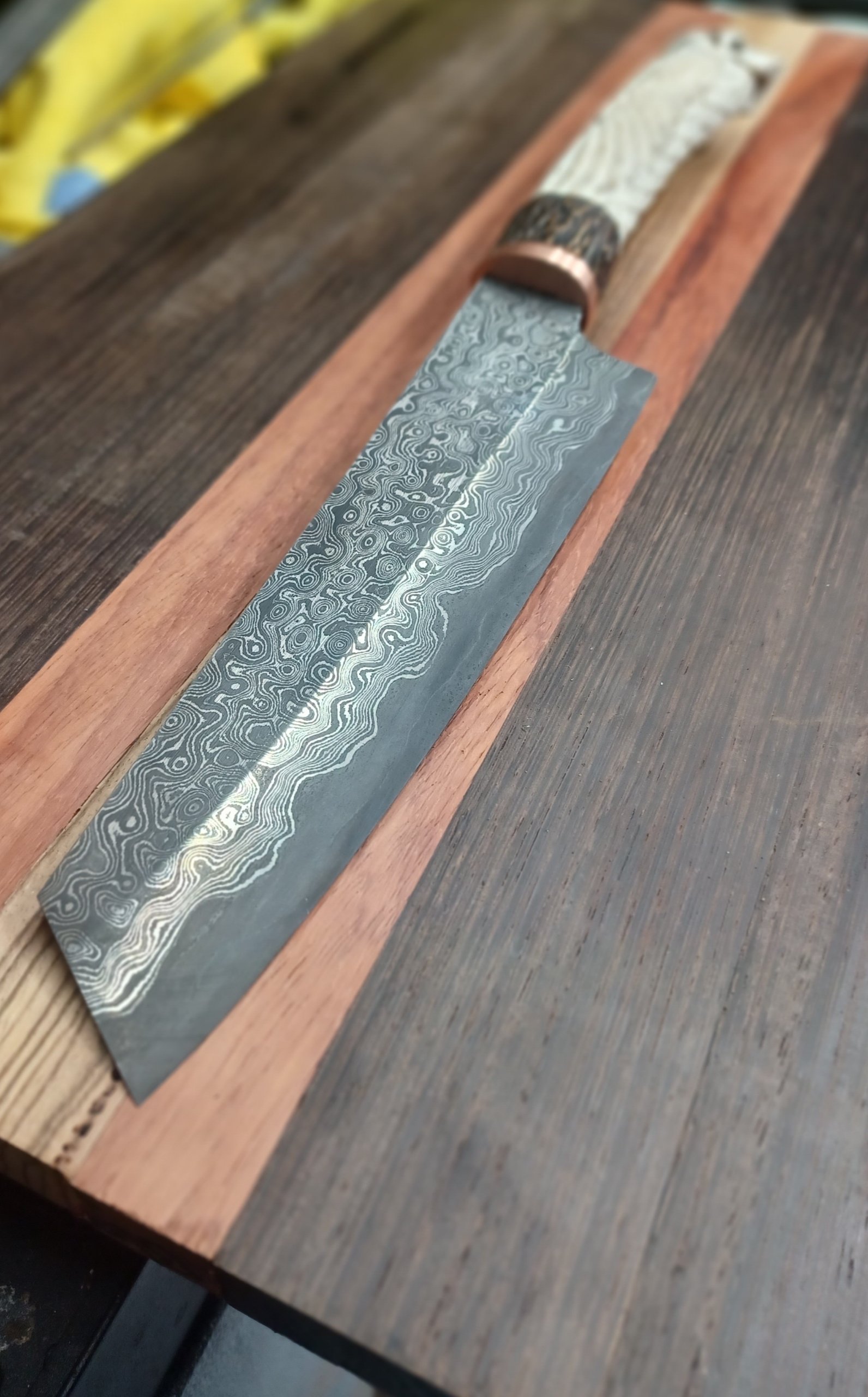 A Japanese-style Damascus steel kitchen knife with a detailed patterned blade, placed on a wooden board.