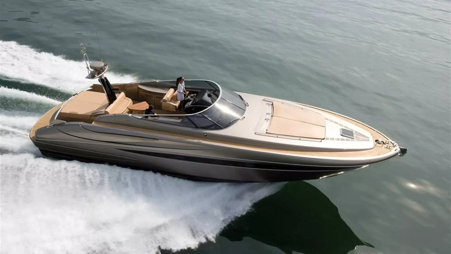 A luxury yacht cruising on the water with two people on board, one steering and the other sitting on a bench.