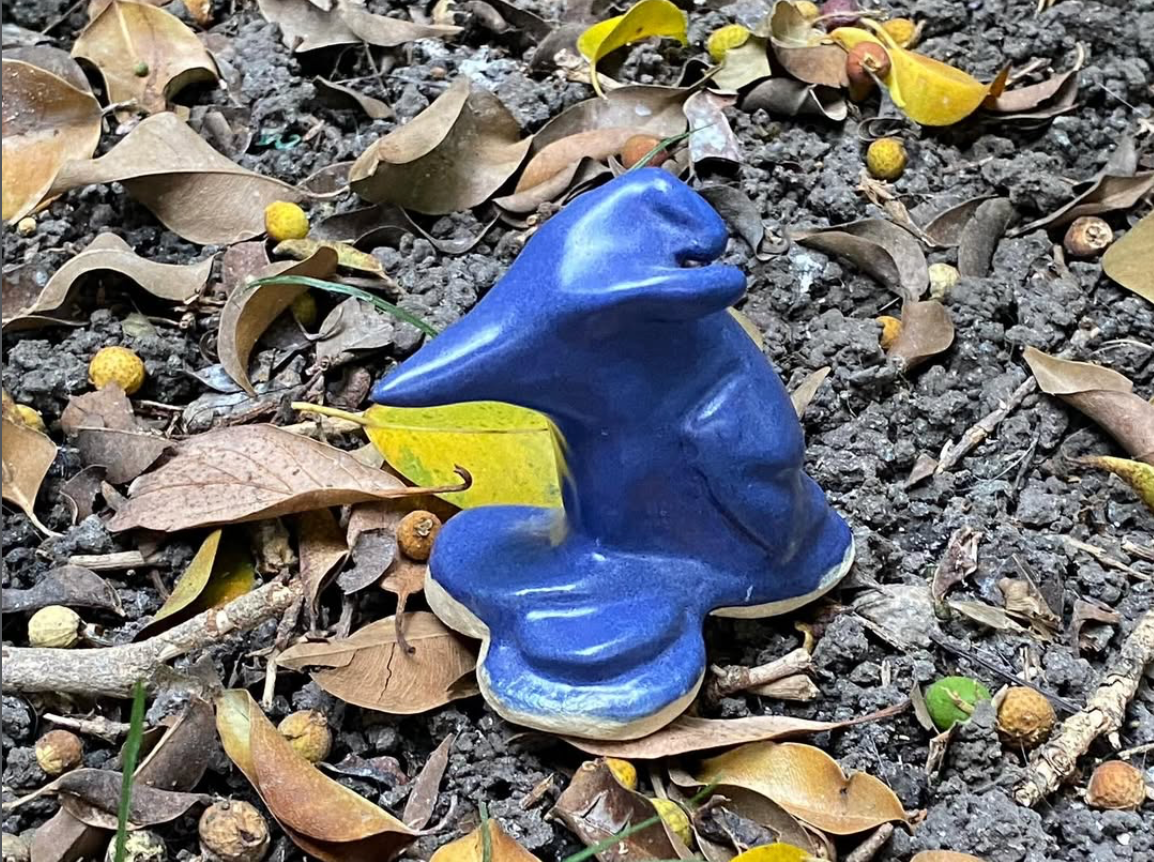 picture of an animal ceramic sculpture in royal blue against a backdrop of twigs and leaves