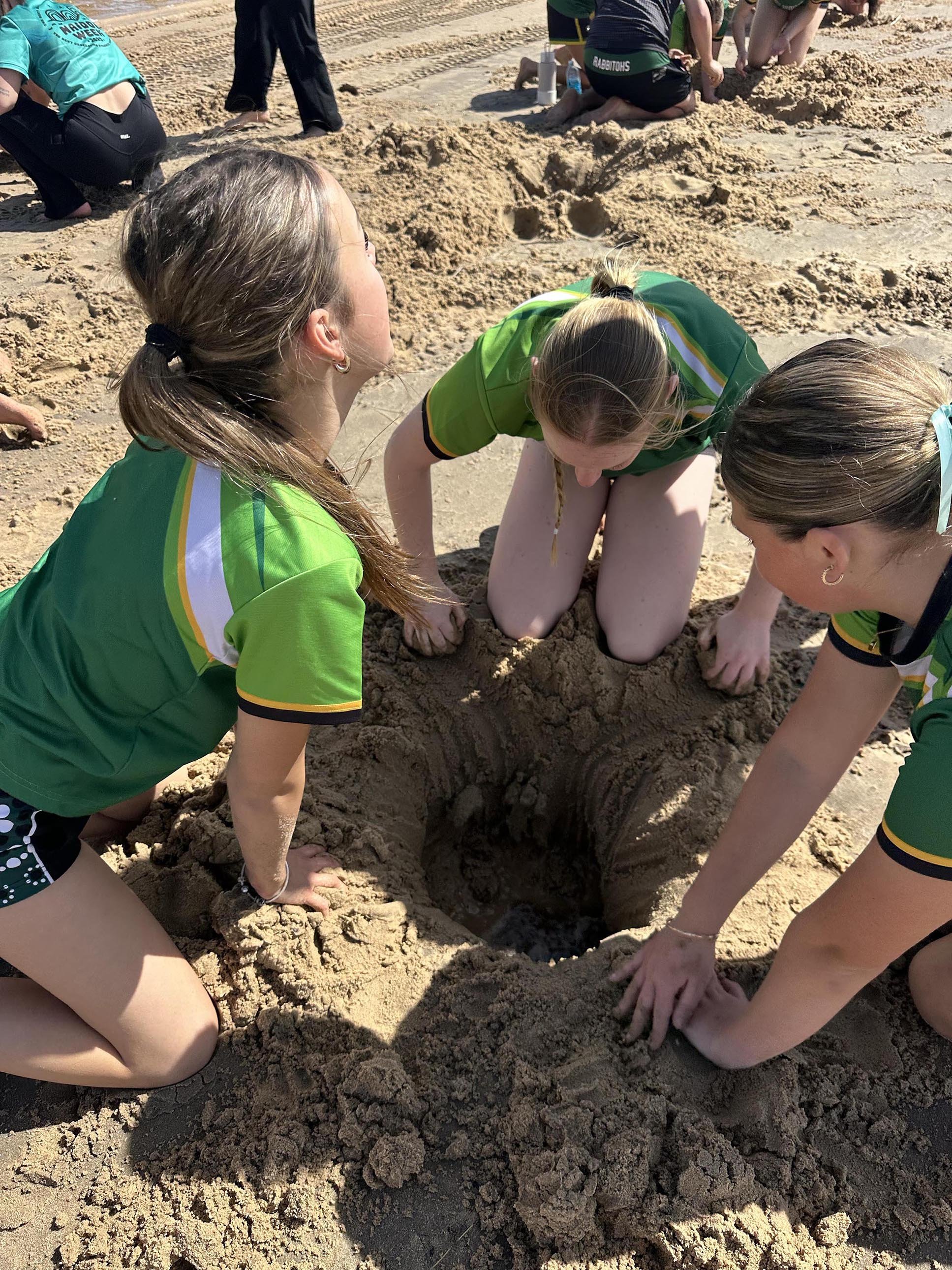 People kneeling on a sandy beach, working together.