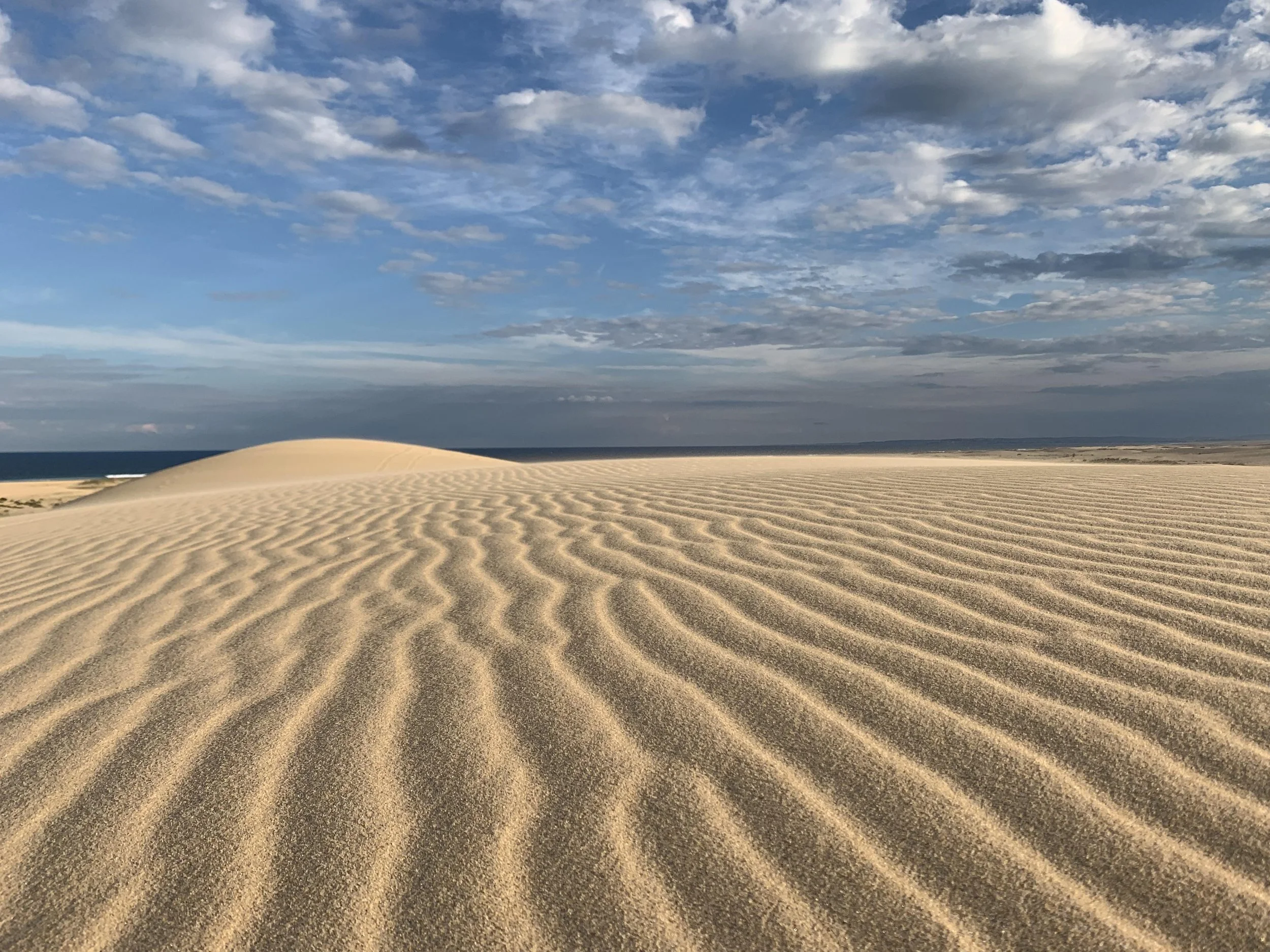 Sand dunes under a partly cloudy sky.