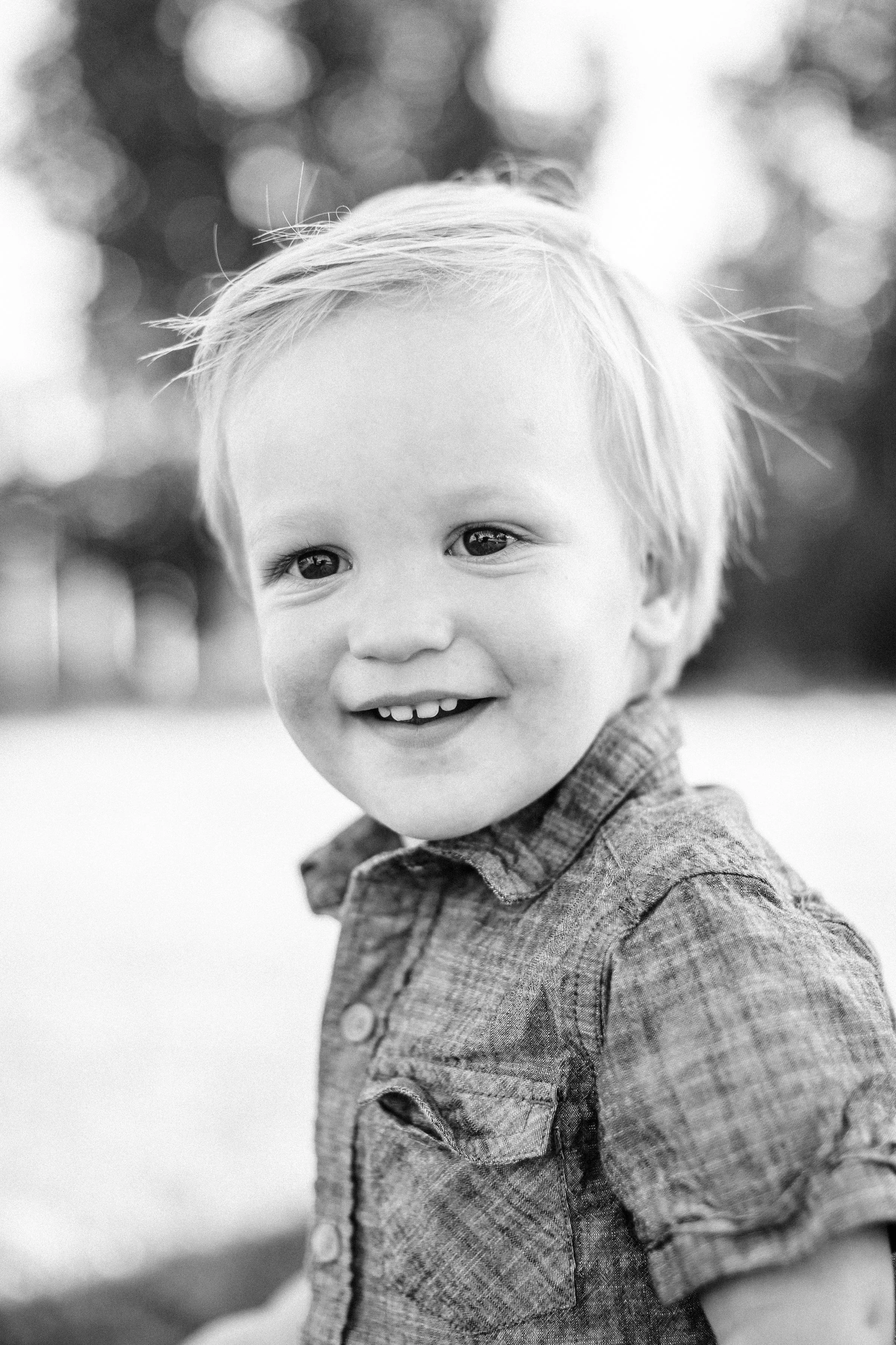 A young boy with light hair smiling outdoors in black and white