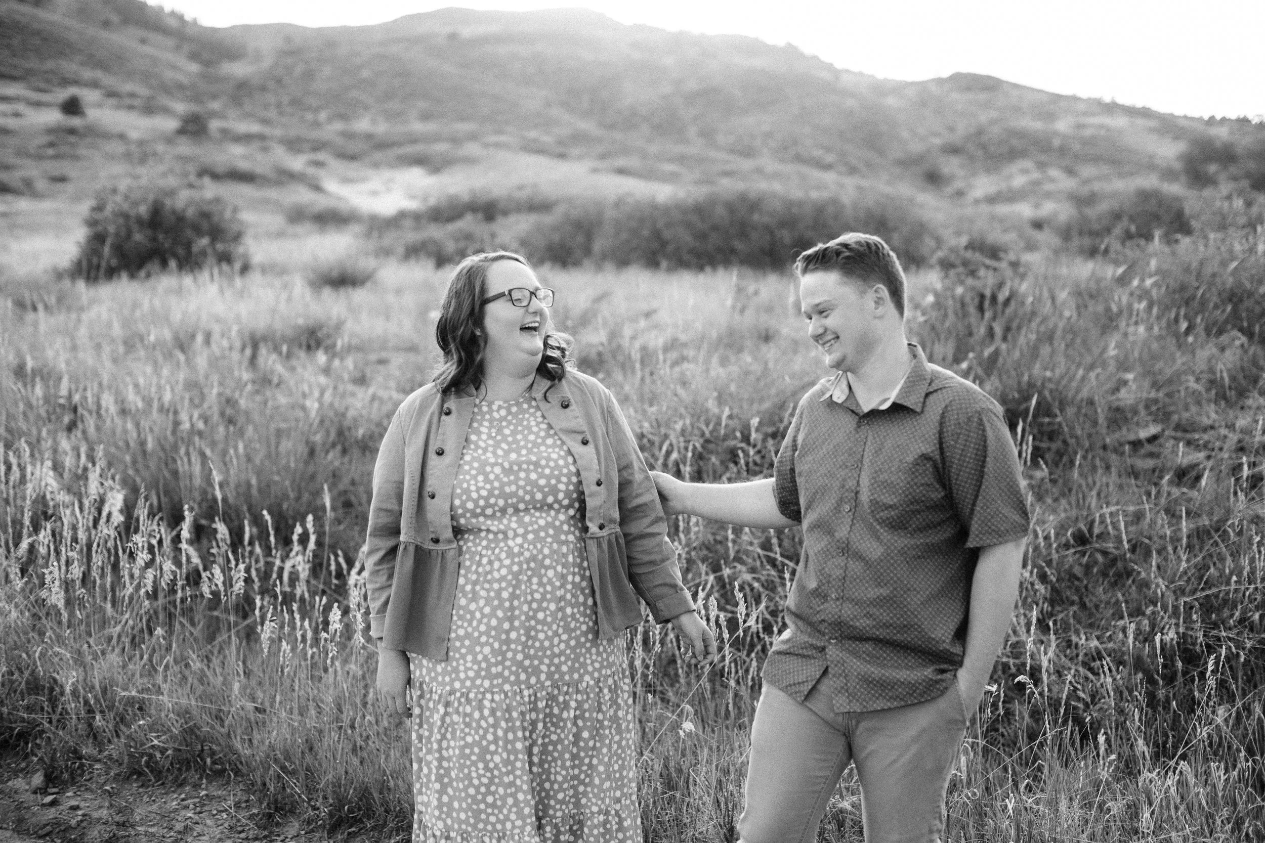 Siblings laughing and talking in a grassy outdoor field with hills in the background in Lory State Park, black and white photo.