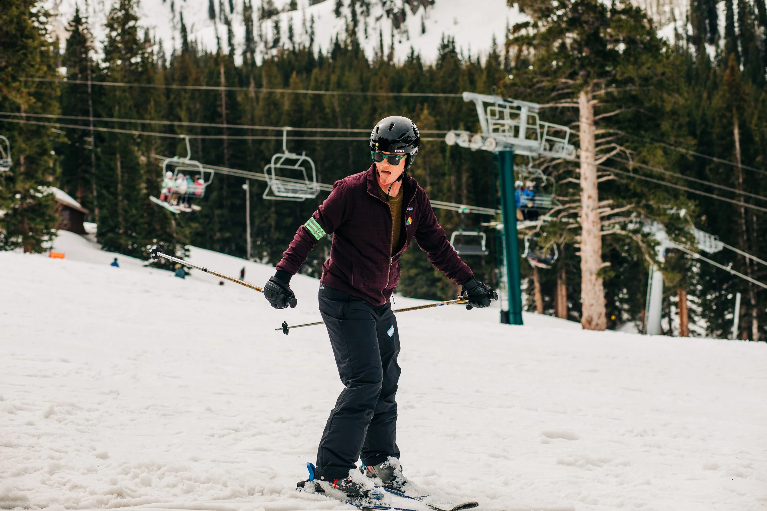 A person skiing on snow with a forested mountain and ski lift in the background.