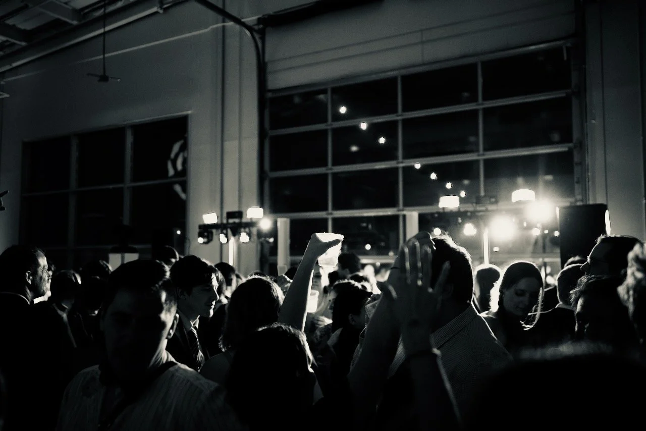 People dancing and socializing at a crowded indoor event or party at night with bright lights and large windows.