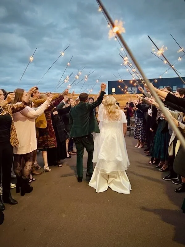 Bride and groom walking through sparklers held by guests during their wedding celebration