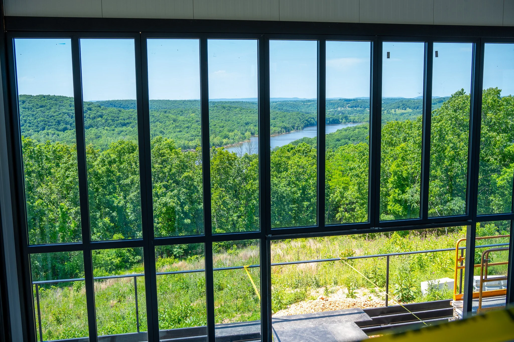 View through large window showing lush green trees, a river, and distant hills under a partly cloudy sky.