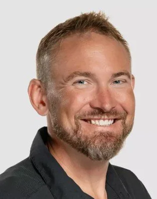A smiling man with short hair and a beard, wearing a black shirt against a plain white background.