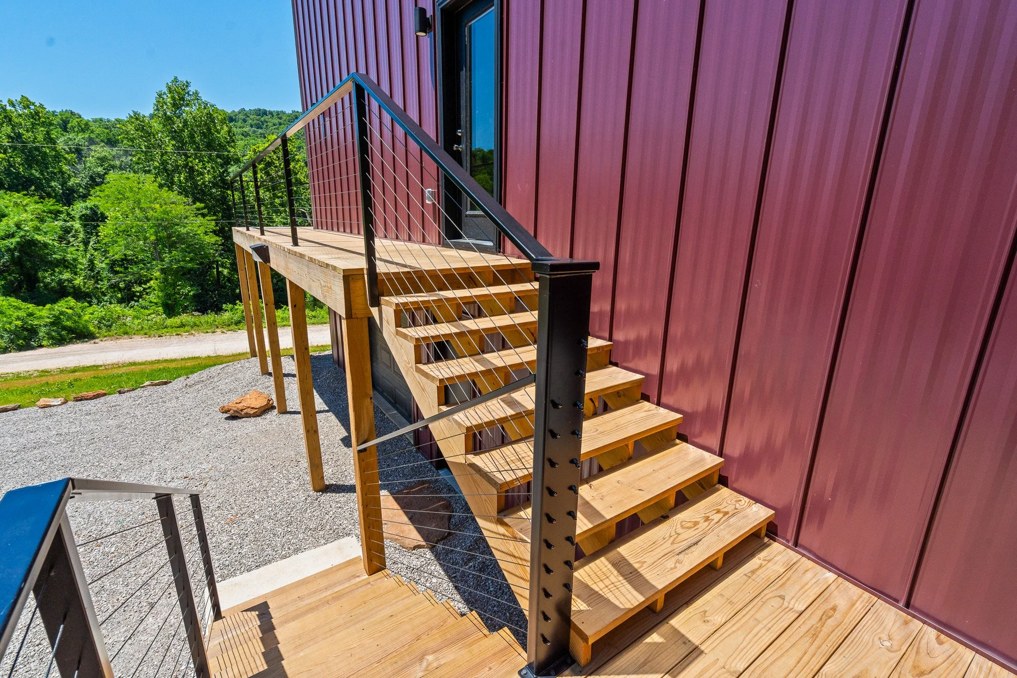 Wooden staircase leading to a door on a modern red building with green trees and blue sky in background.