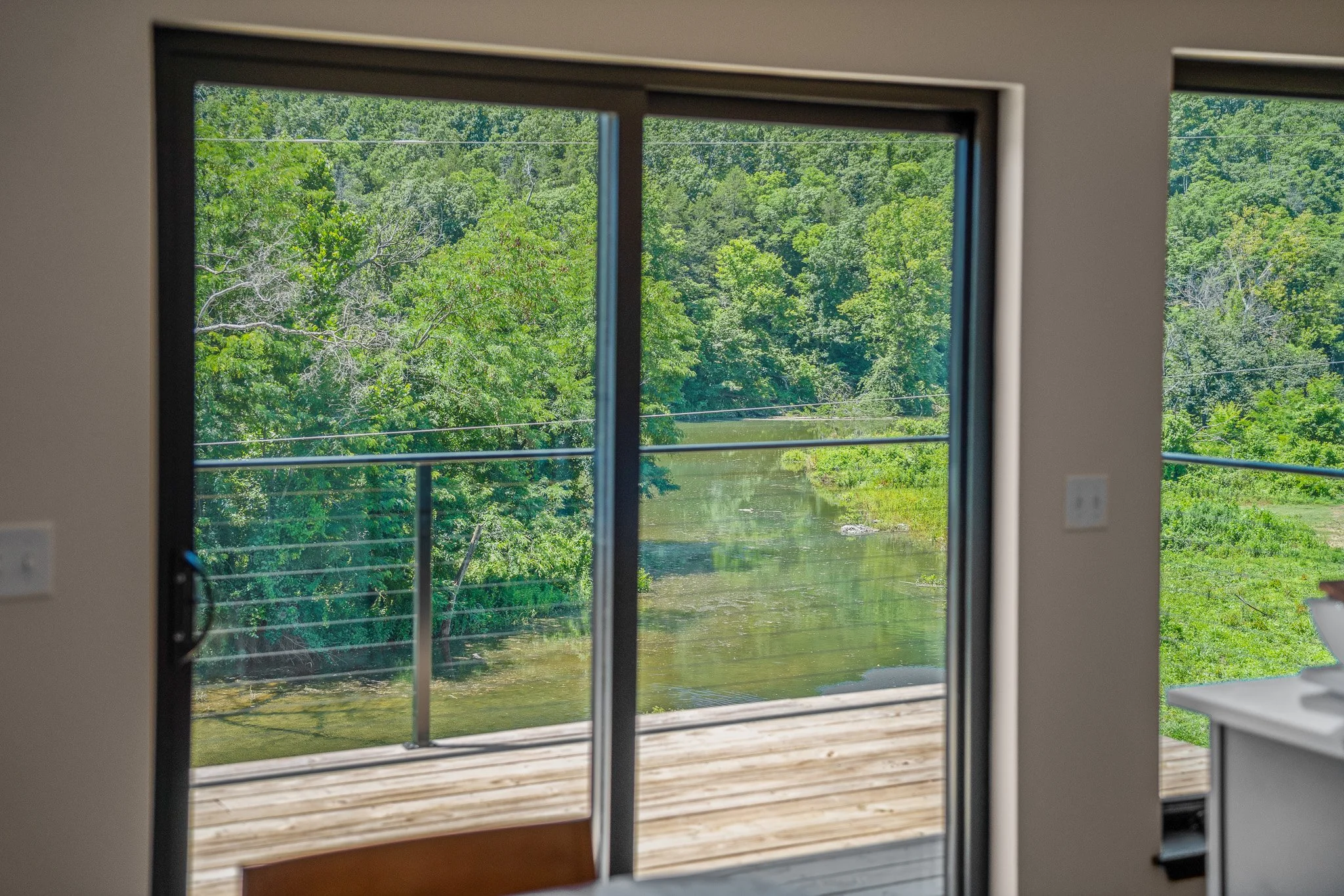 View through sliding glass door showing a lush green forest and water body outside, with part of an interior room visible including a white counter or table.