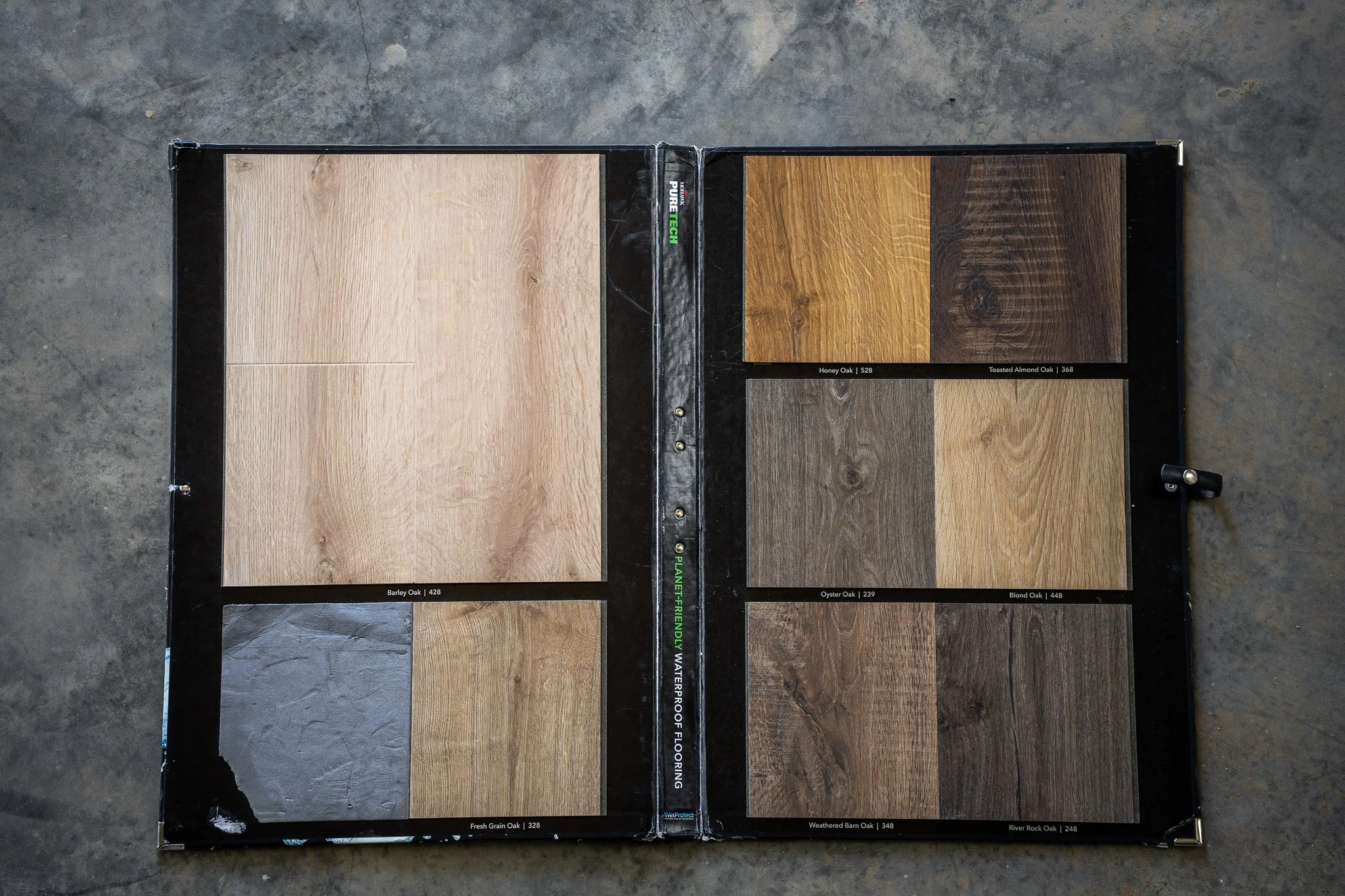 A display book showing samples of hardwood flooring in various shades including light, medium, and dark wood tones.