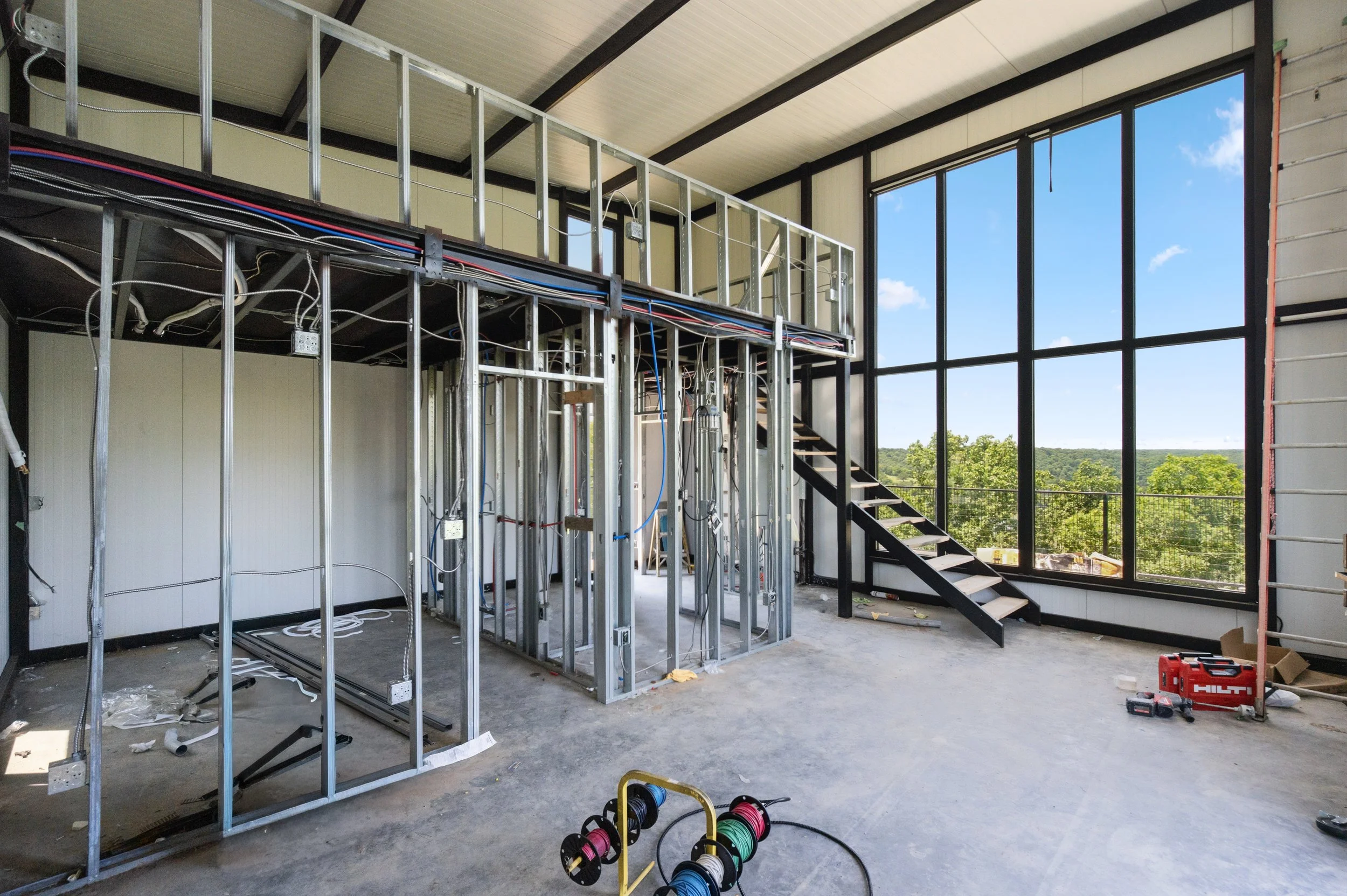 Interior of a building under construction with metal framing, large windows, and tools scattered on the floor.