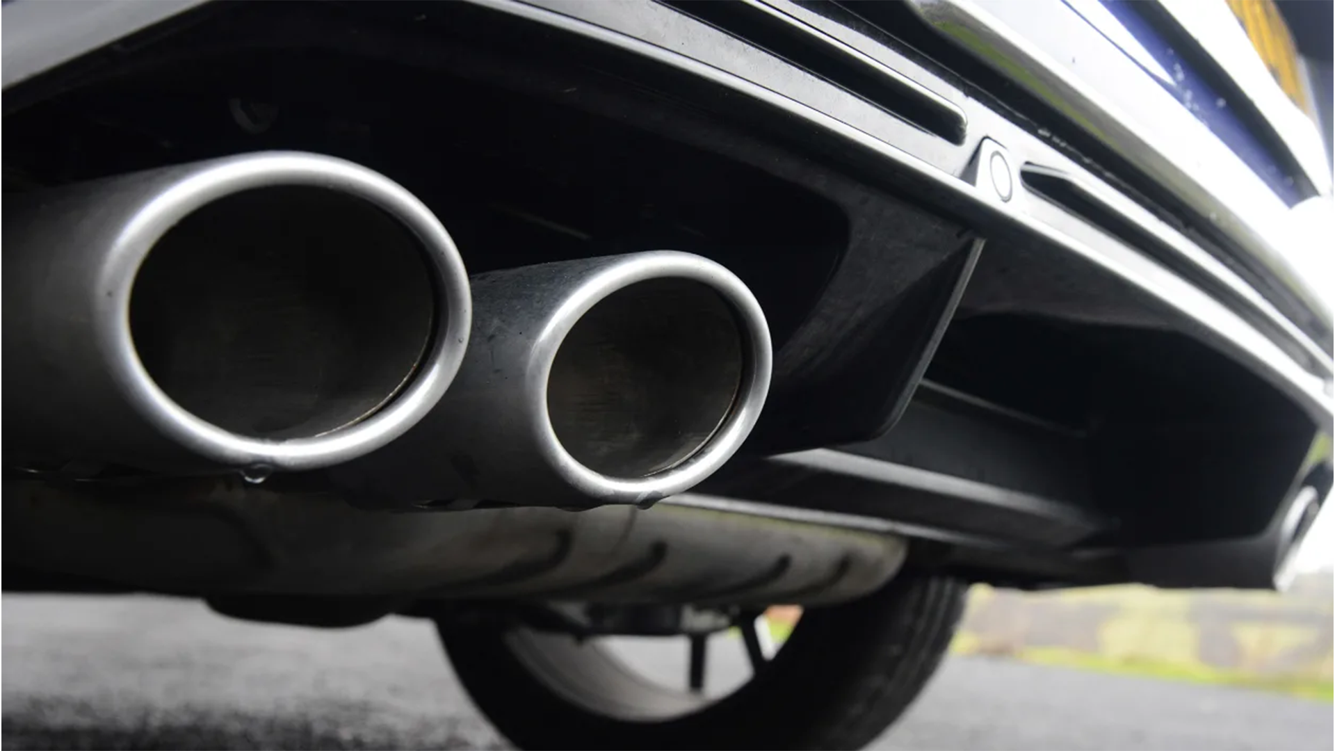 Close-up of dual car exhaust pipes beneath the rear bumper of a vehicle.