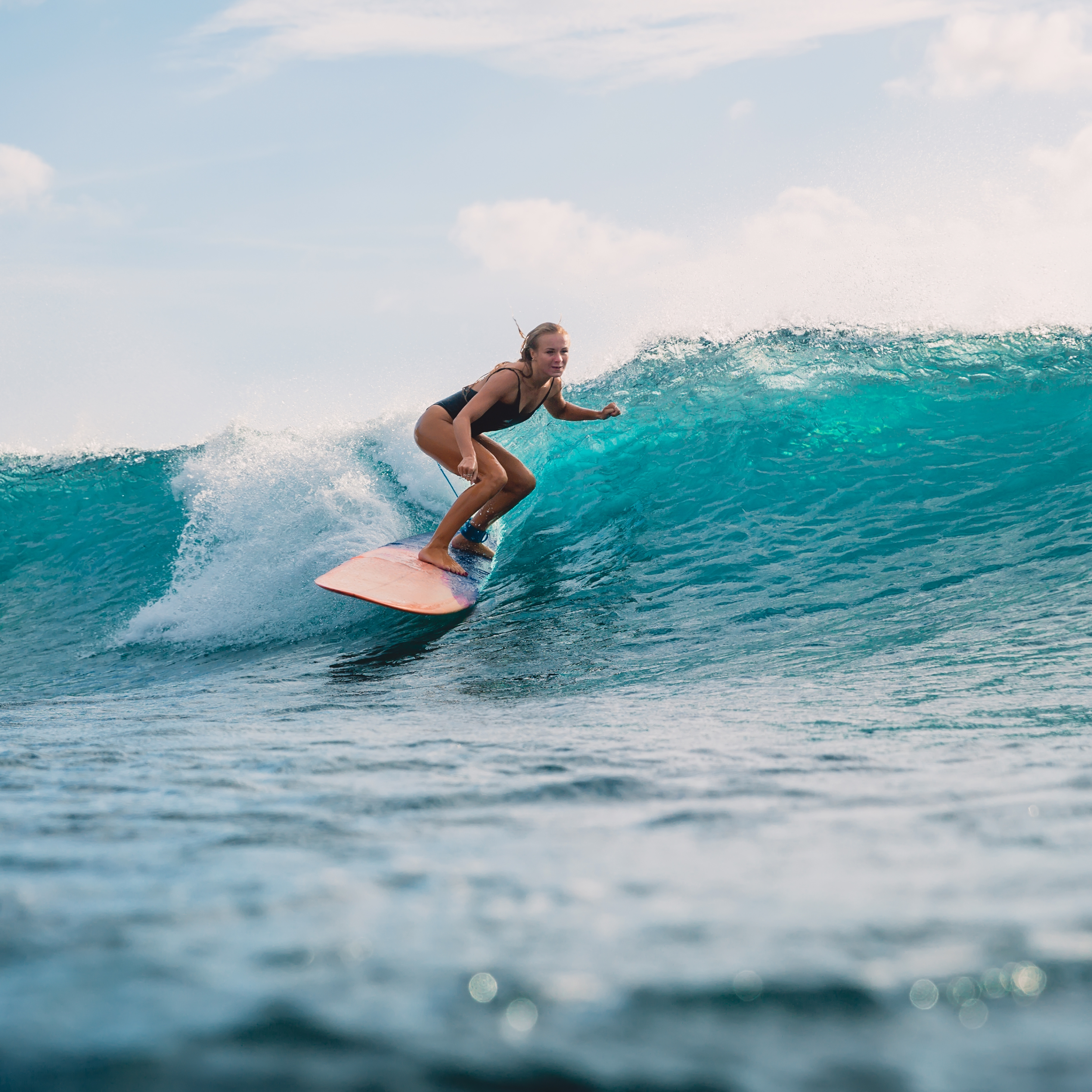 A woman surfing on a wave in the ocean under a blue sky.
