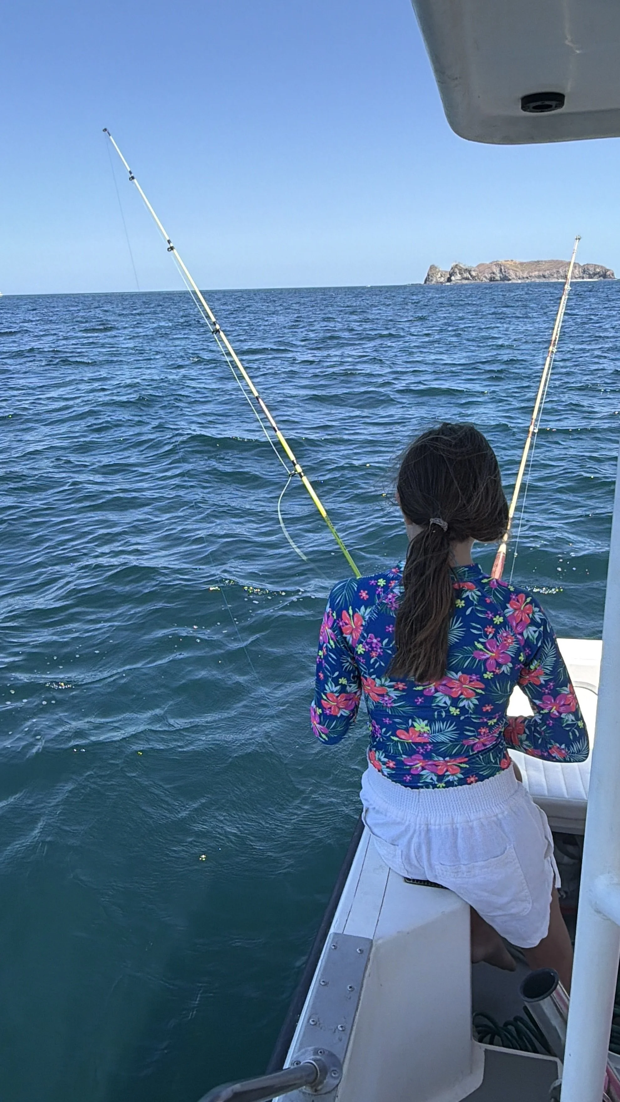 A girl on a boat fishing in the ocean with a distant island in the background.