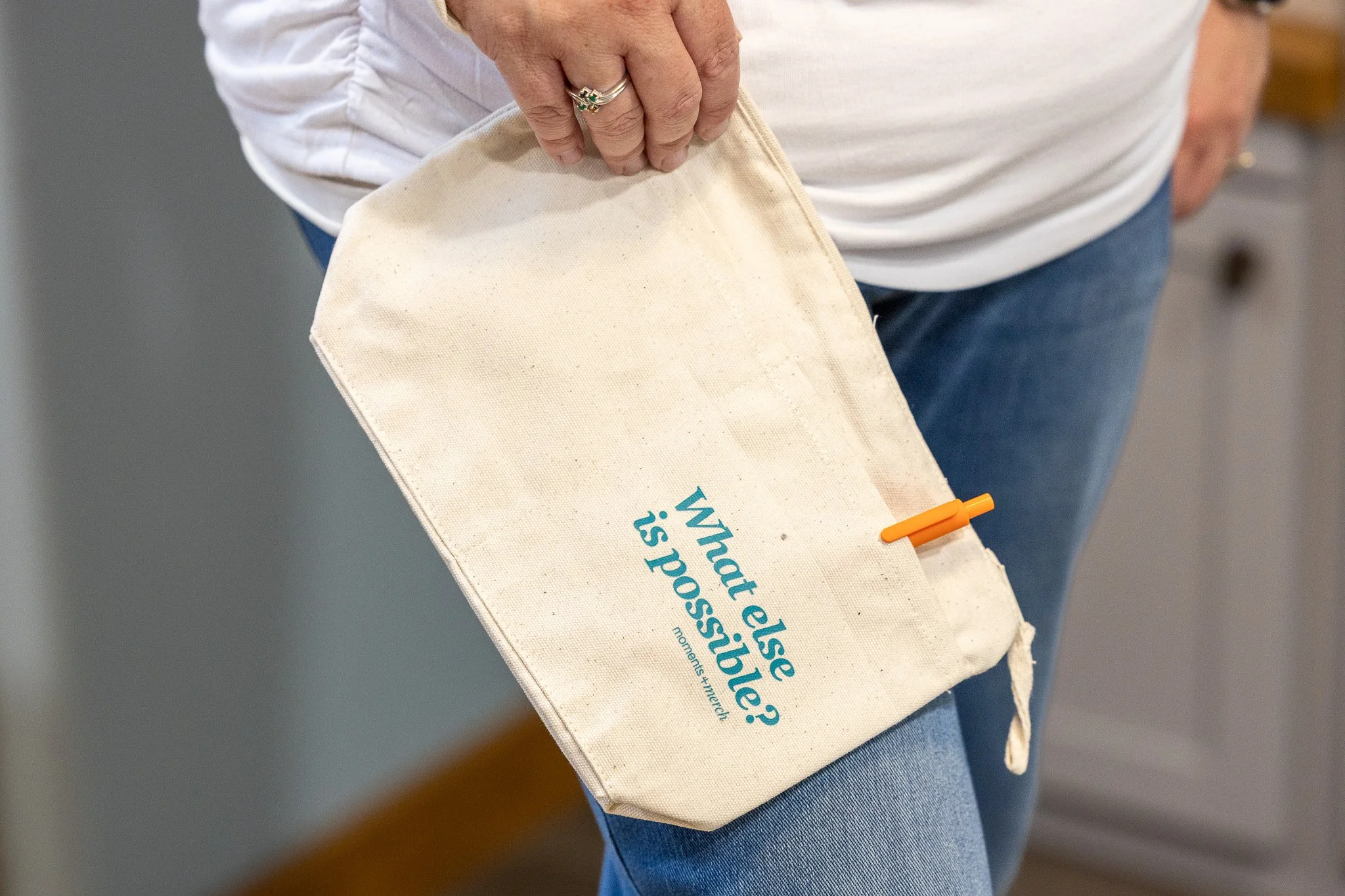 Cream colored pouch with What Else is Possible? and an orange pen.