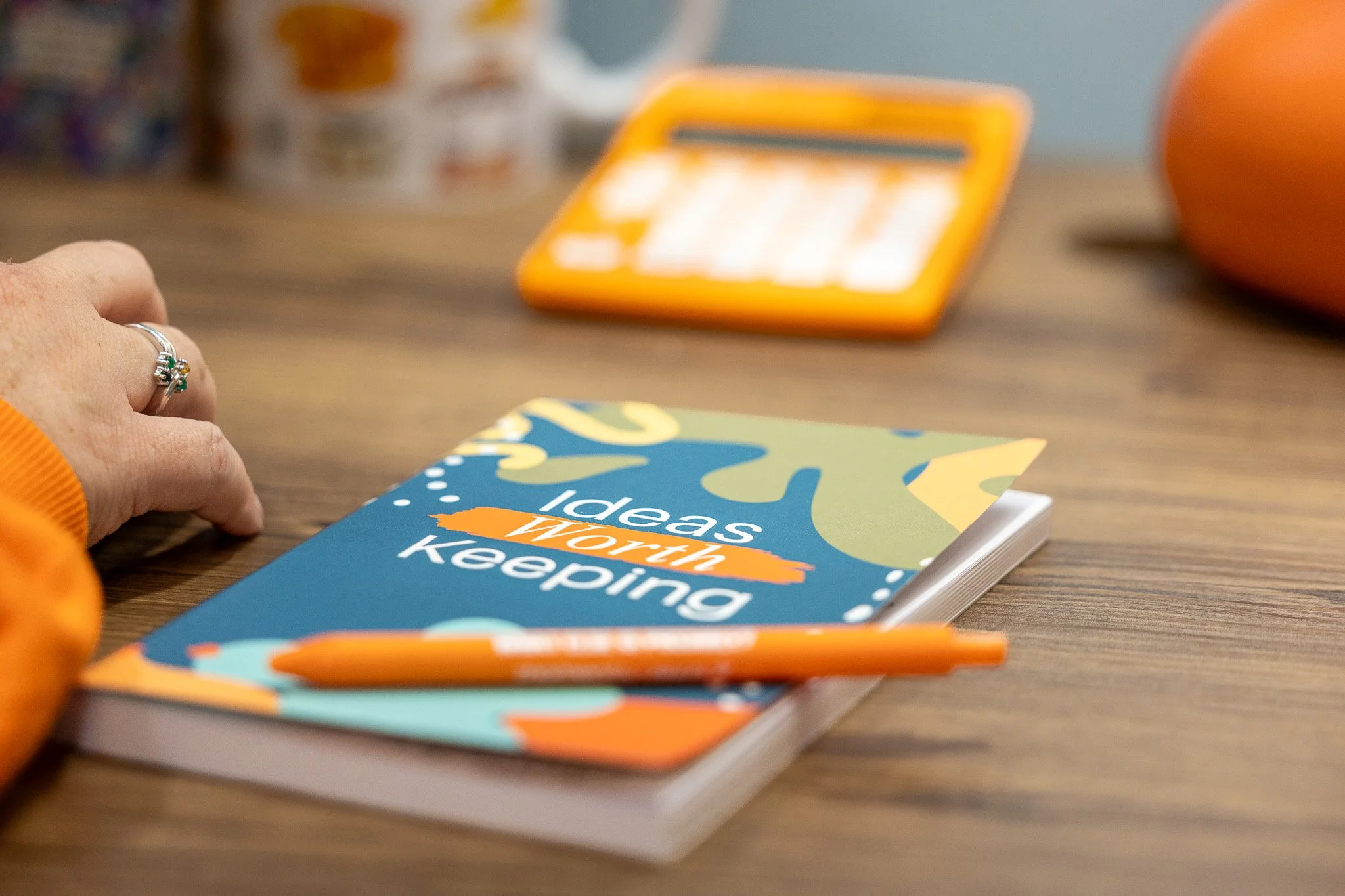 Notebook that says Ideas Worth Keeping and orange pen on a desk.