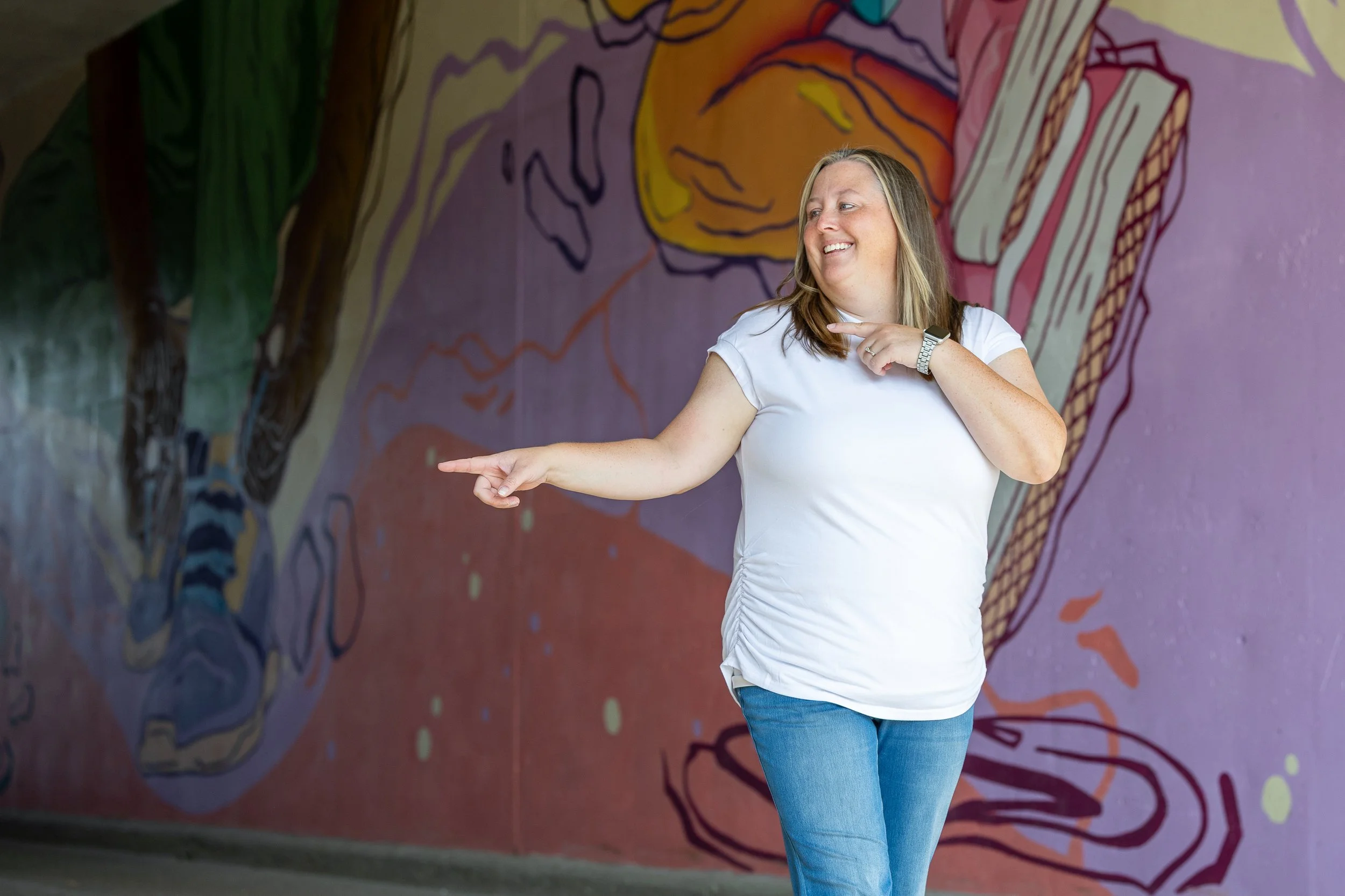 Girl in White T-shirt pointing with mural behind her.