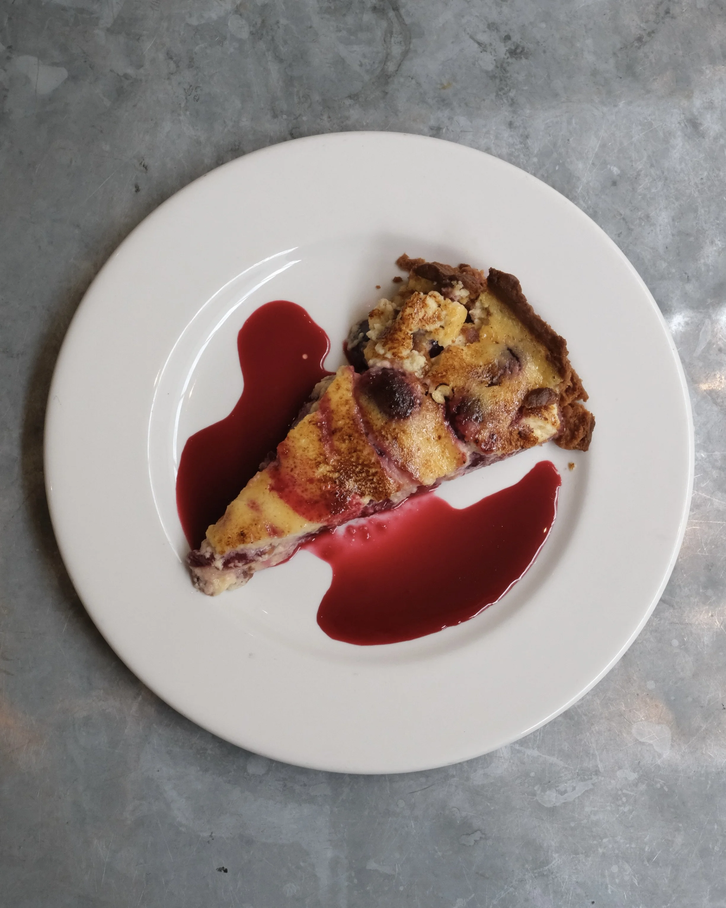 A cherry tart on a white plate against a grey background