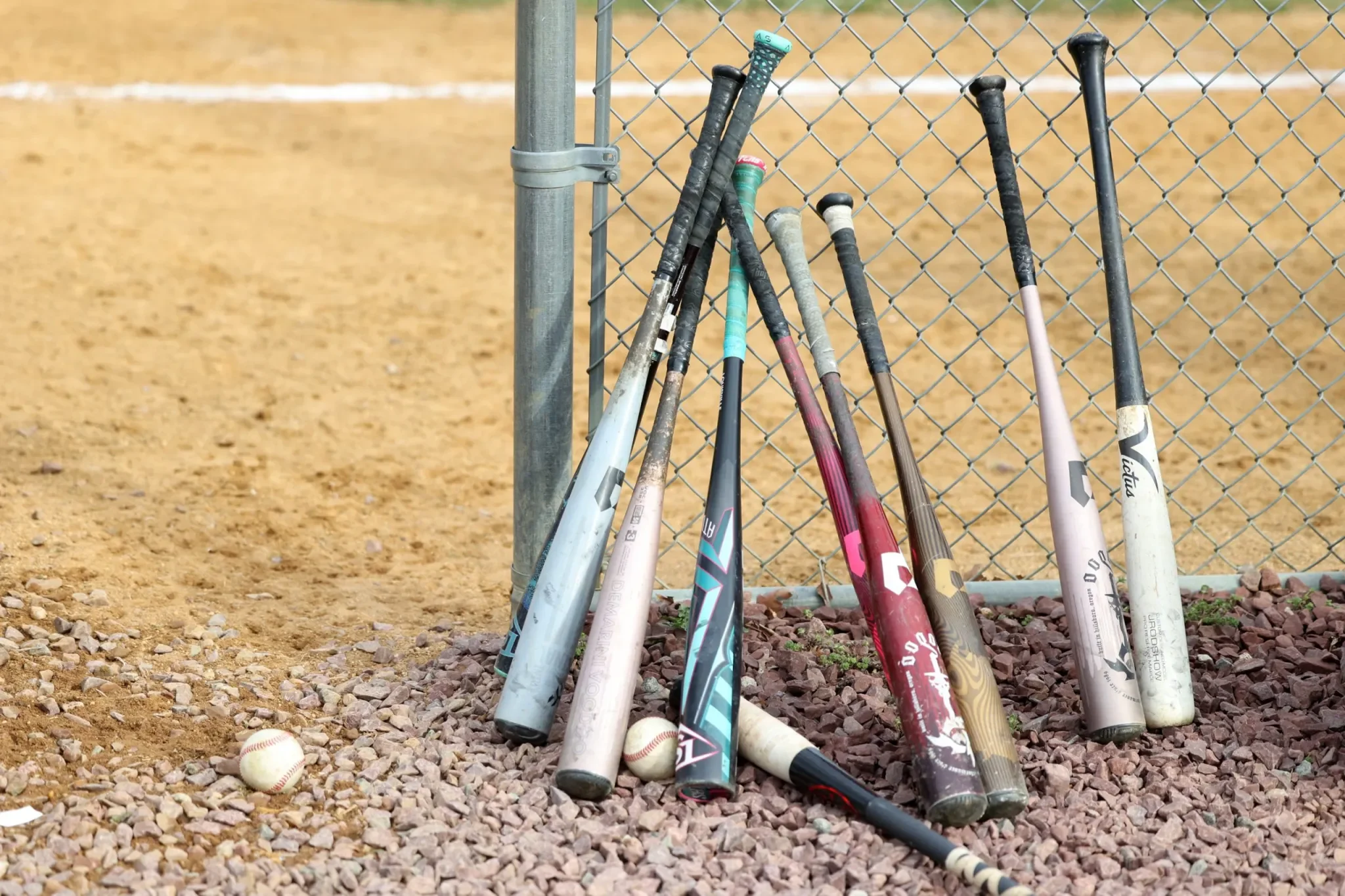 Baseball bats on a fence with baseballs on the ground