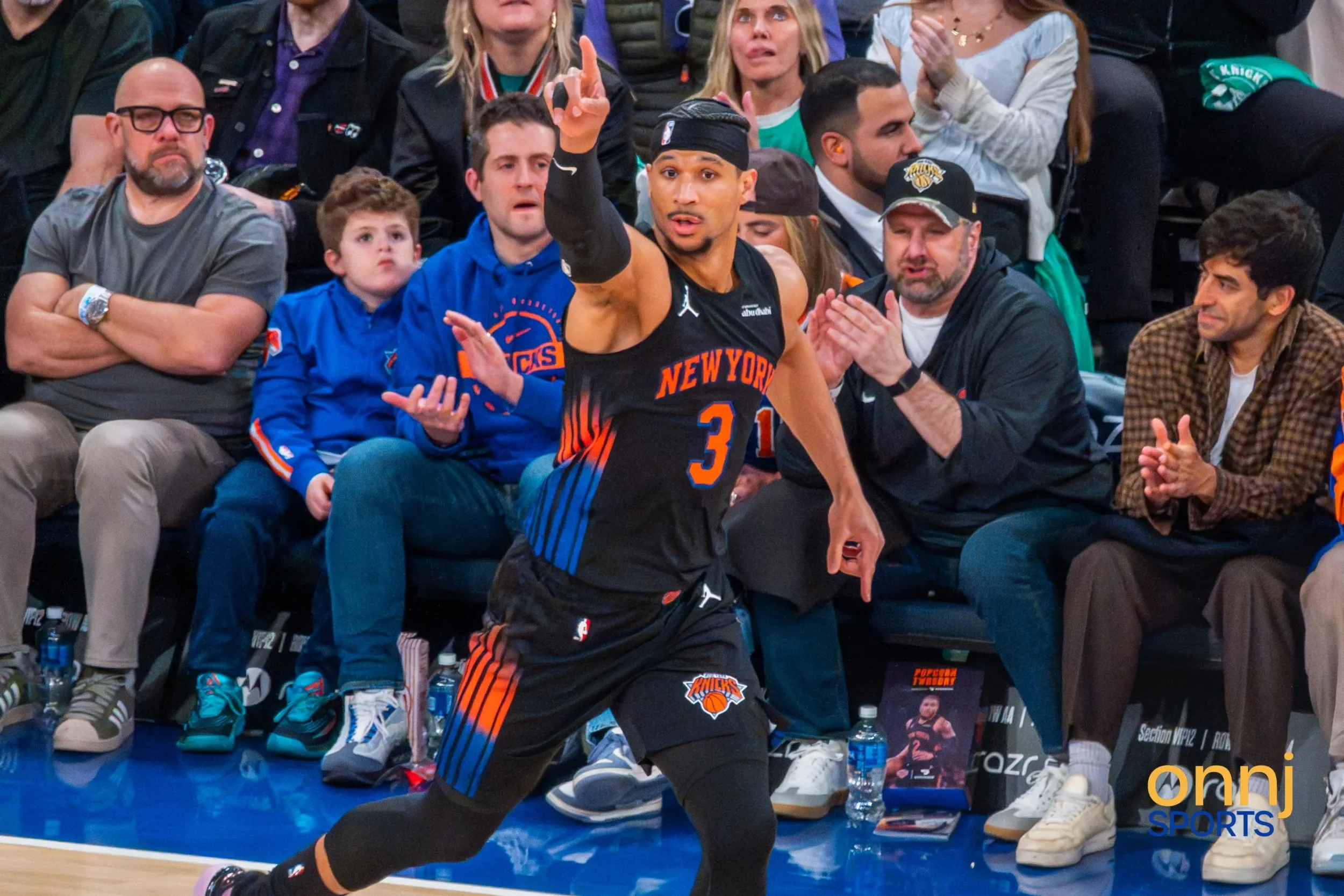 Josh Hart in a black New York Knicks uniform wearing the number 3 is pointing on the court during a game, with spectators watching from the background.