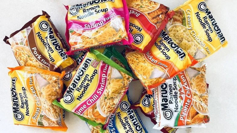 Several different flavors of Maruchan instant ramen noodle soups scattered on a surface, including pork, shrimp, chicken, and chili shrimp flavors.