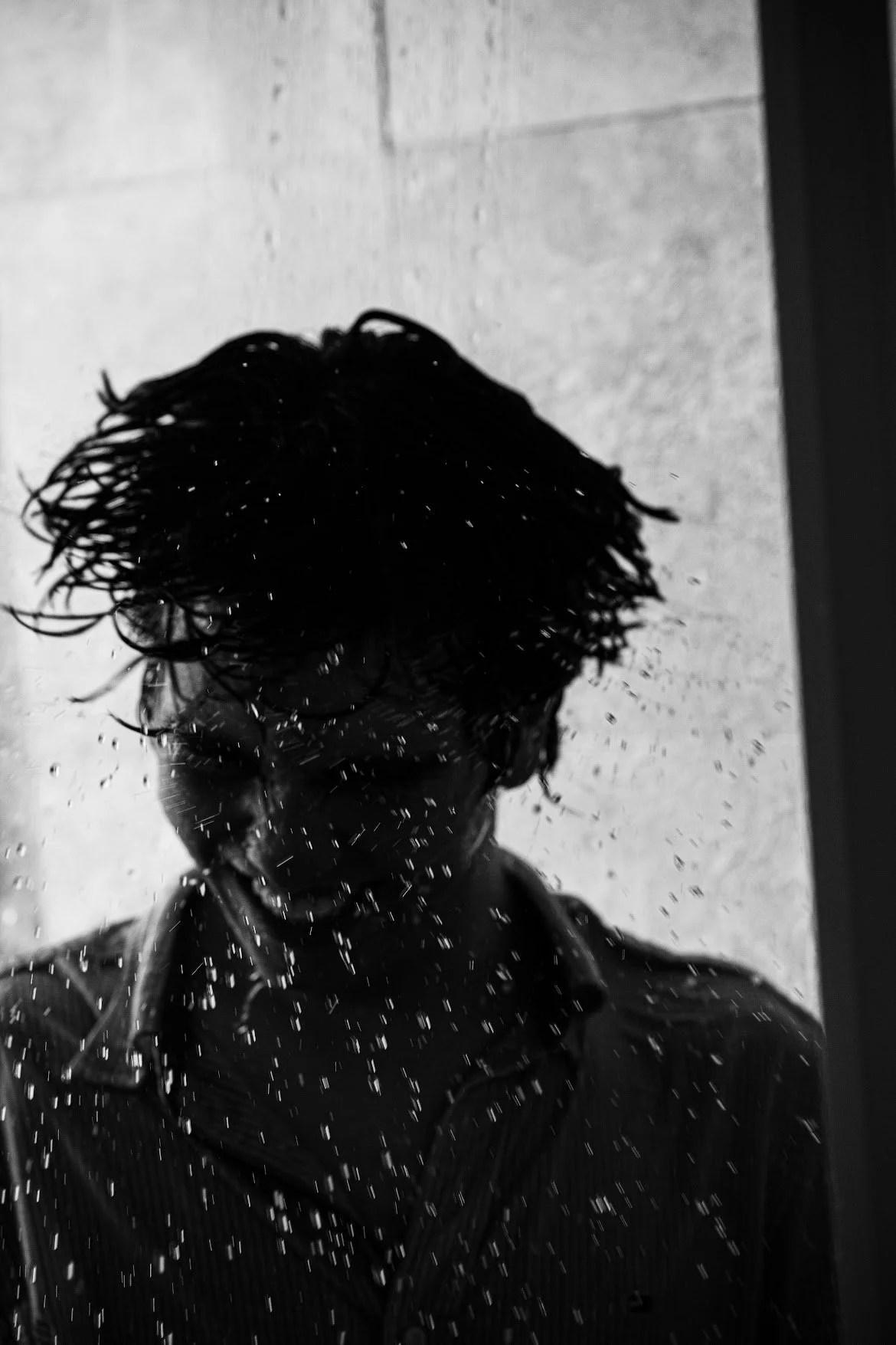 Ray Maldonado with wet hair and glasses looking at a mirror, with spray of water droplets on the mirror.