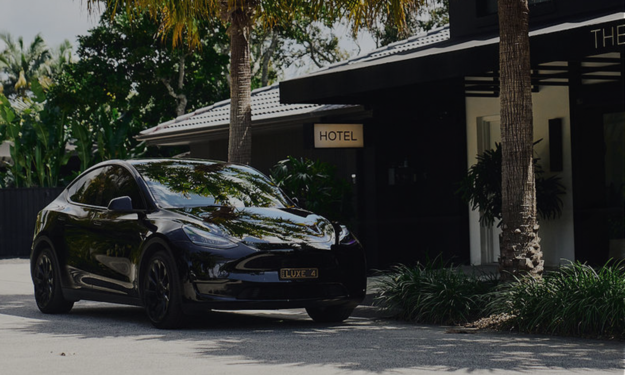A black luxury sports car parked outside a modern hotel with palm trees and lush greenery around.