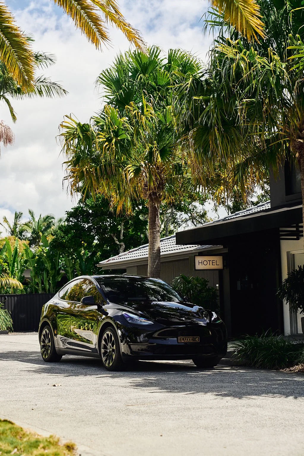Black sports car parked outside a hotel with tropical palm trees and lush greenery in the background.