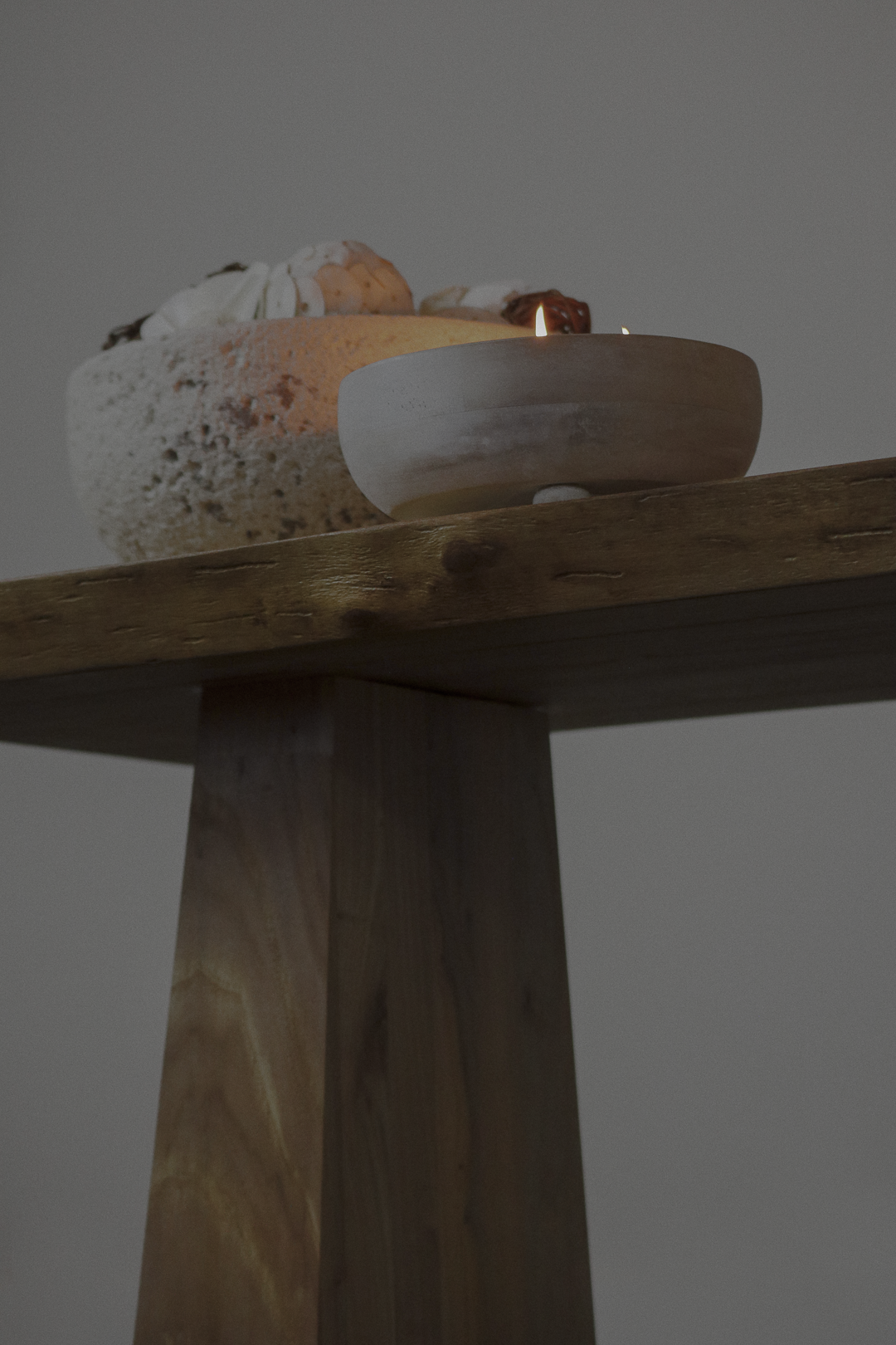 Close-up of a wooden table with a candle and a decorative object on top, against a plain background.