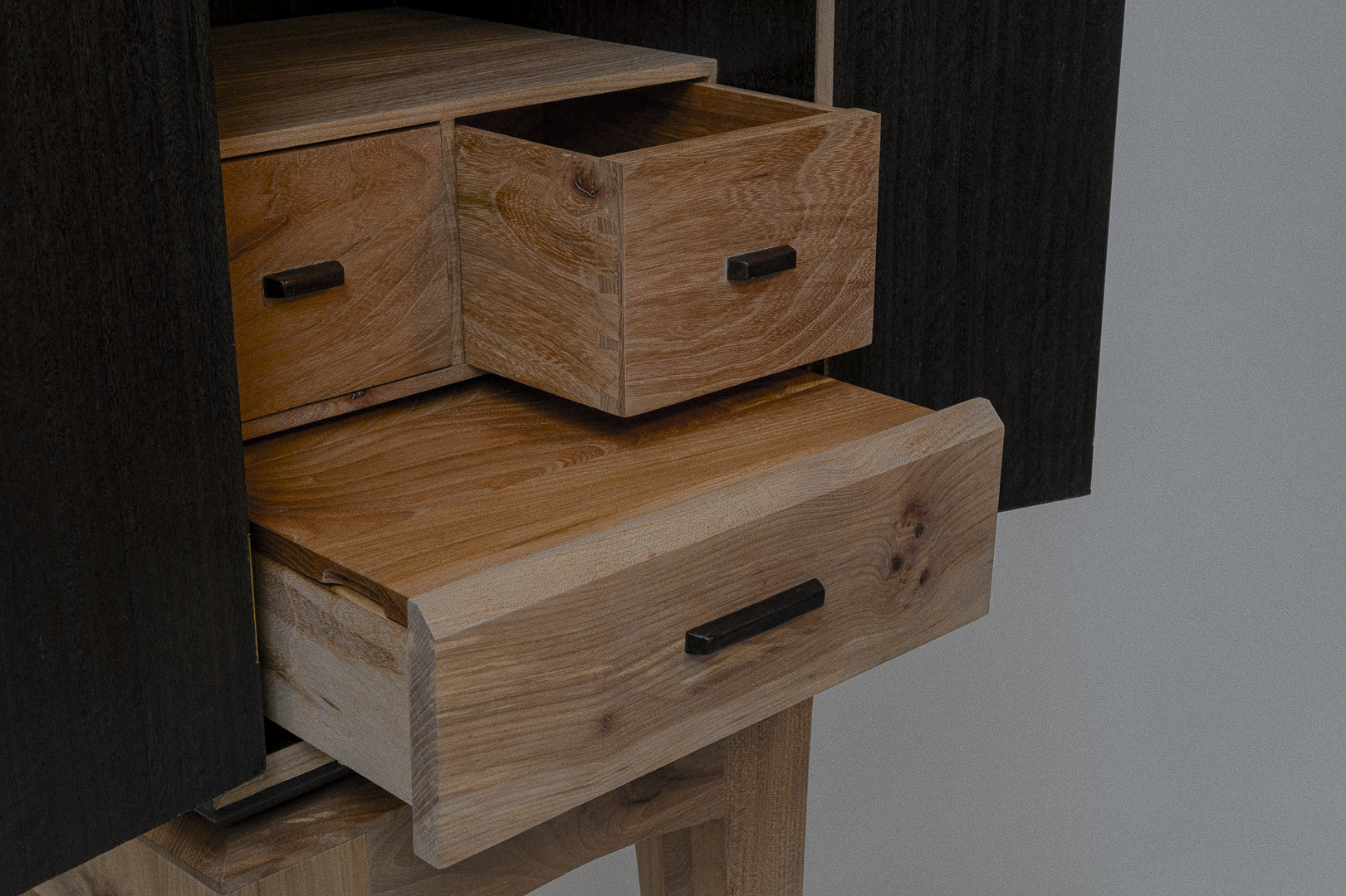 Close-up view of a wooden whiskey or liquor cabinet dresser with multiple open drawers showing natural wood grain and black handles.