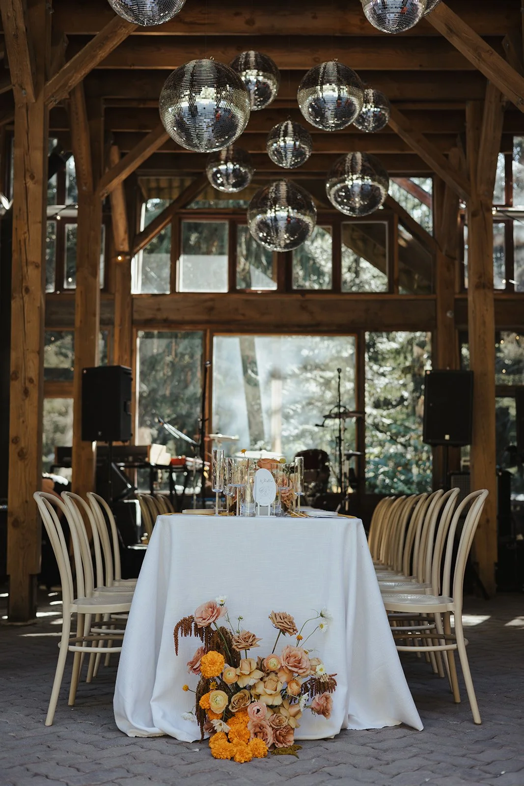 Wedding reception table setup in a rustic wooden barn with disco balls hanging from the ceiling, floral arrangements on the table and adding color to the setting.