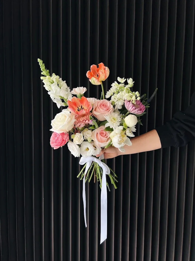 A bouquet of various flowers including roses, tulips, and other blooms, held by a person against a black textured background.