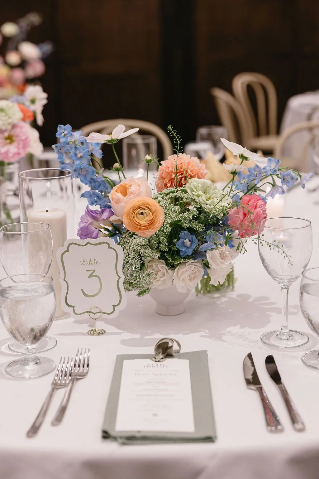 Elegant table setting at a wedding reception with a flower centerpiece, glassware, cutlery, and a table number card for table 3.
