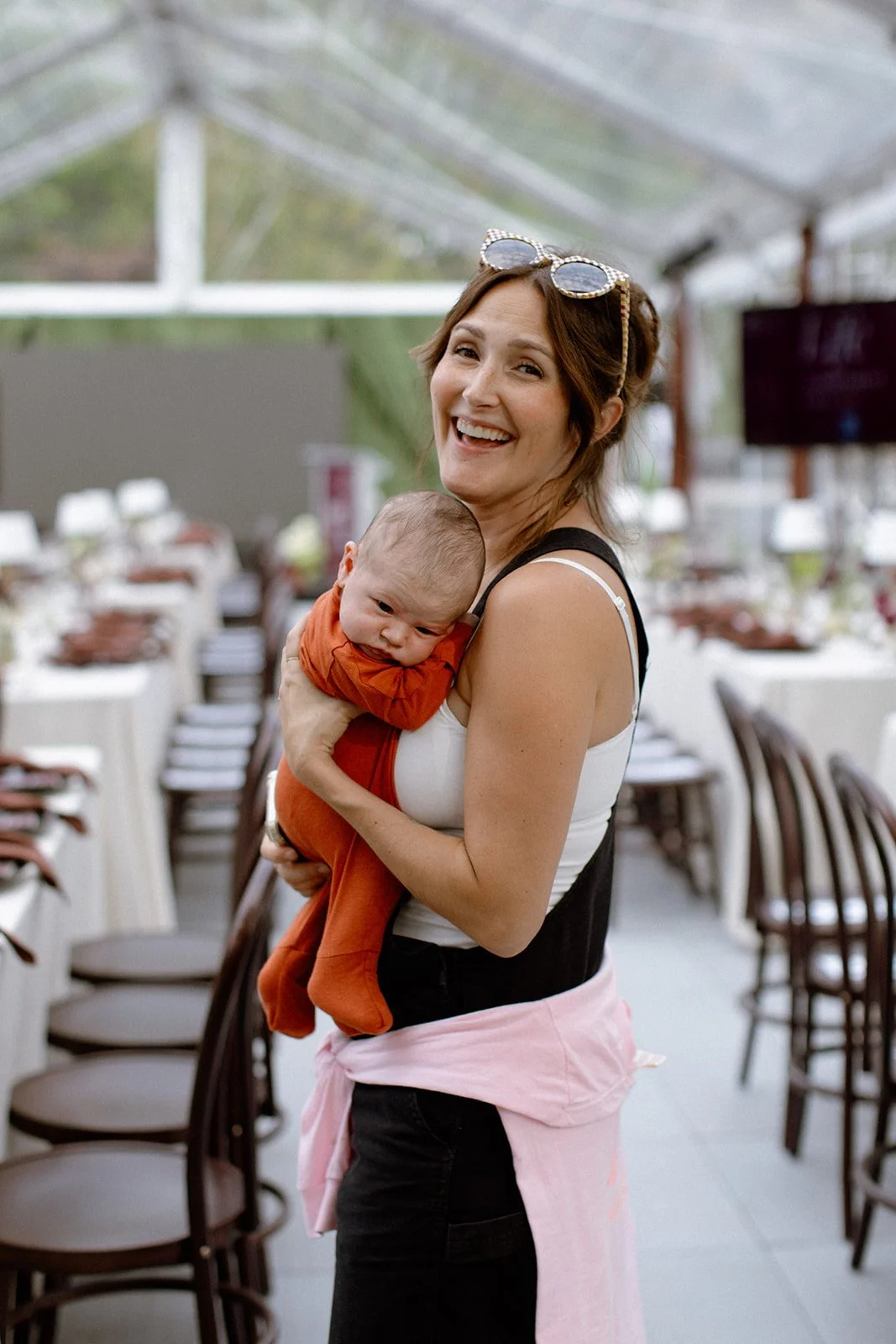 A woman holding a baby in an outdoor dining area, smiling at the camera.