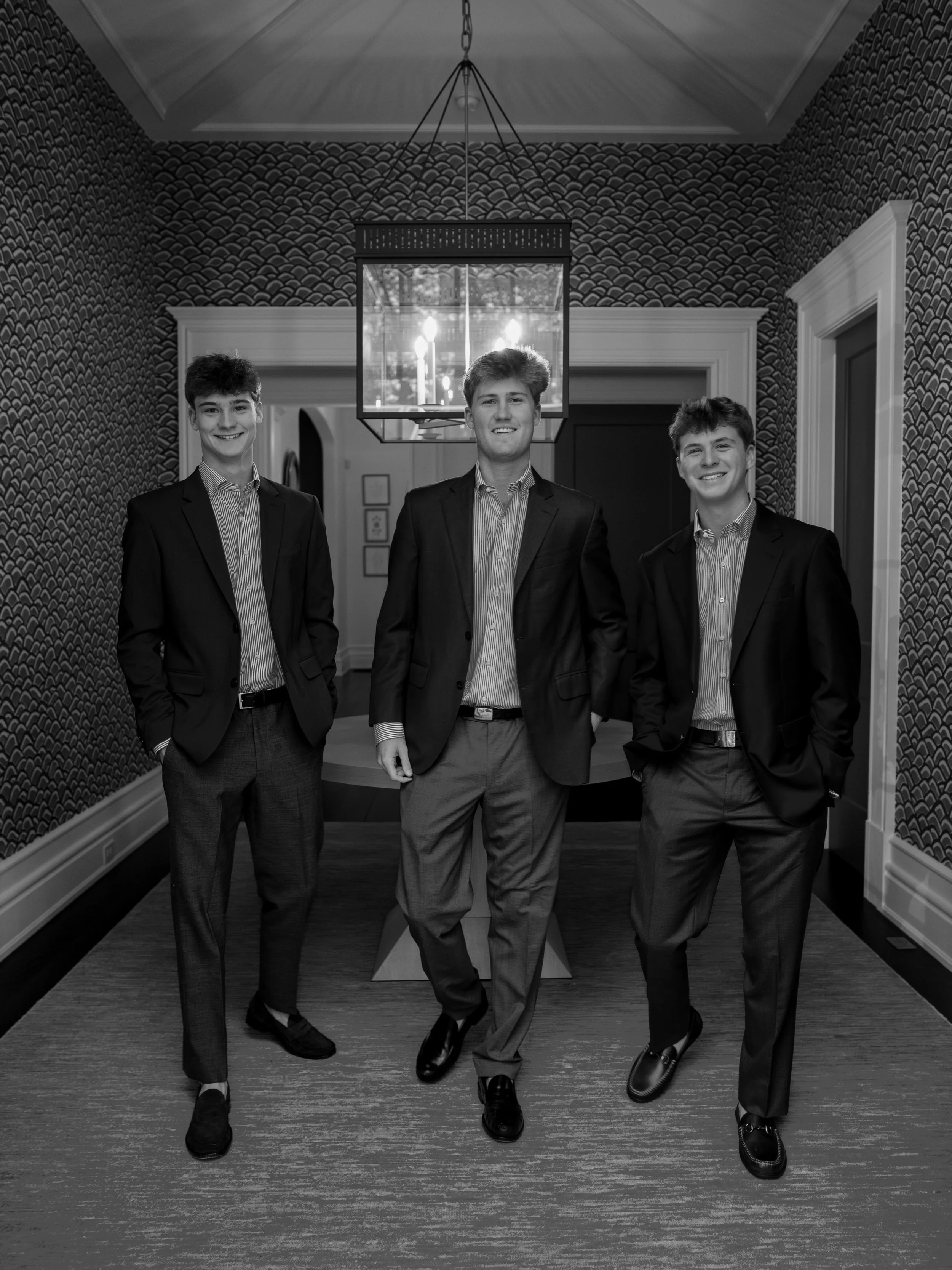 Three young men in suits standing in a decorated room, smiling at the camera.