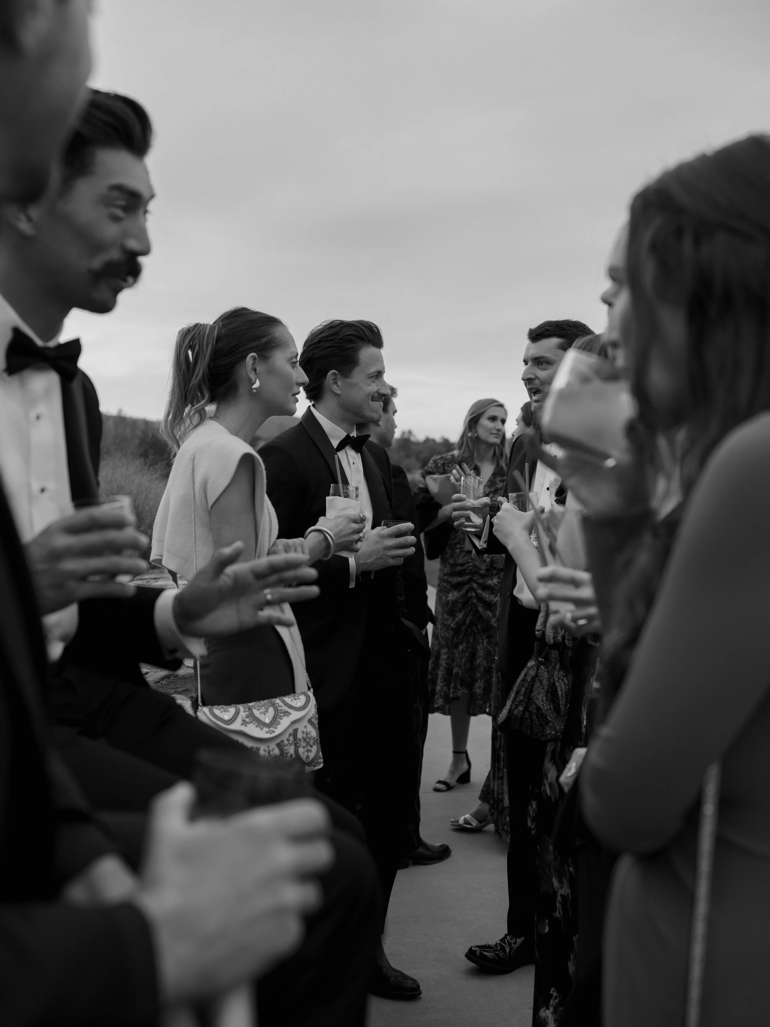 Group of people in formal attire socializing and drinking outside at twilight.