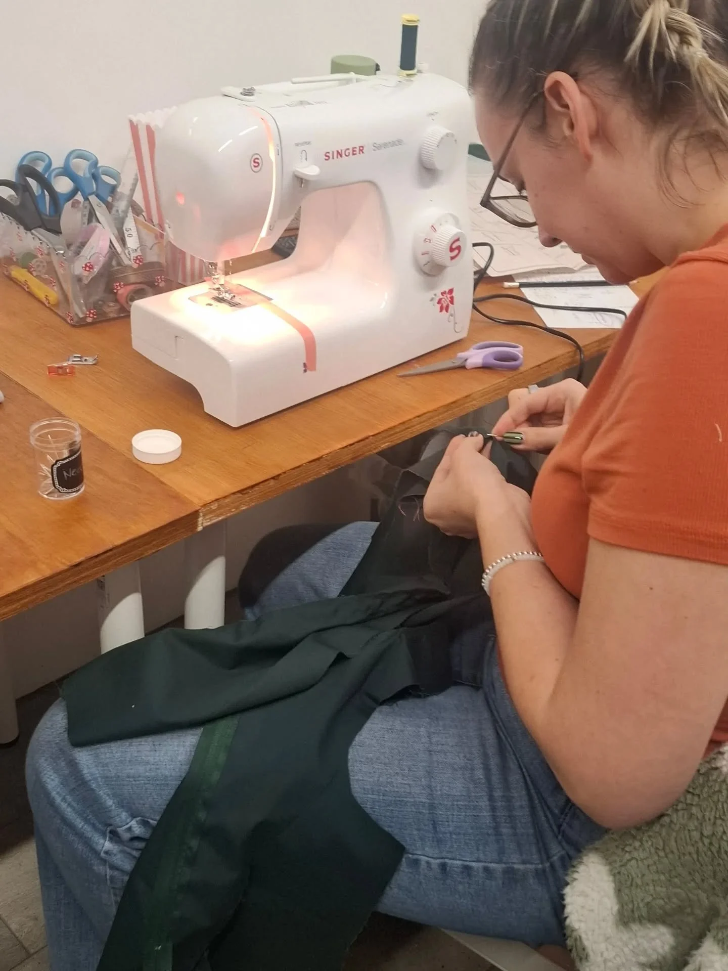 A woman sewing fabric on a sewing machine at a wooden table.