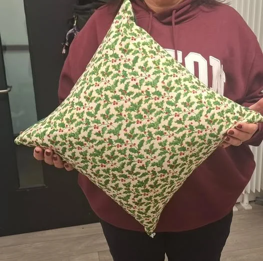 Person holding a decorative pillow with a Christmas-themed pattern of holly leaves and red berries.