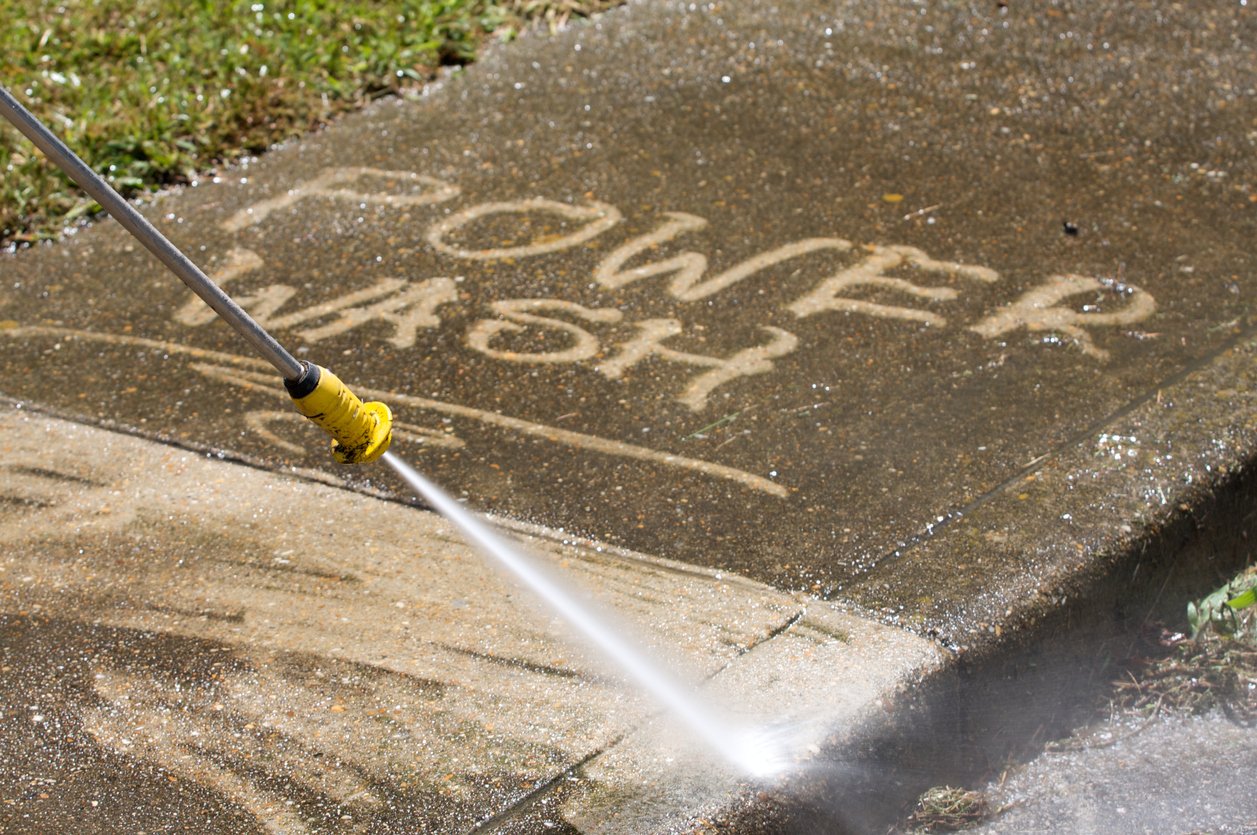 A person power washing a concrete sidewalk with the words 'LOVE' and 'JESUS' written in the wet surface.