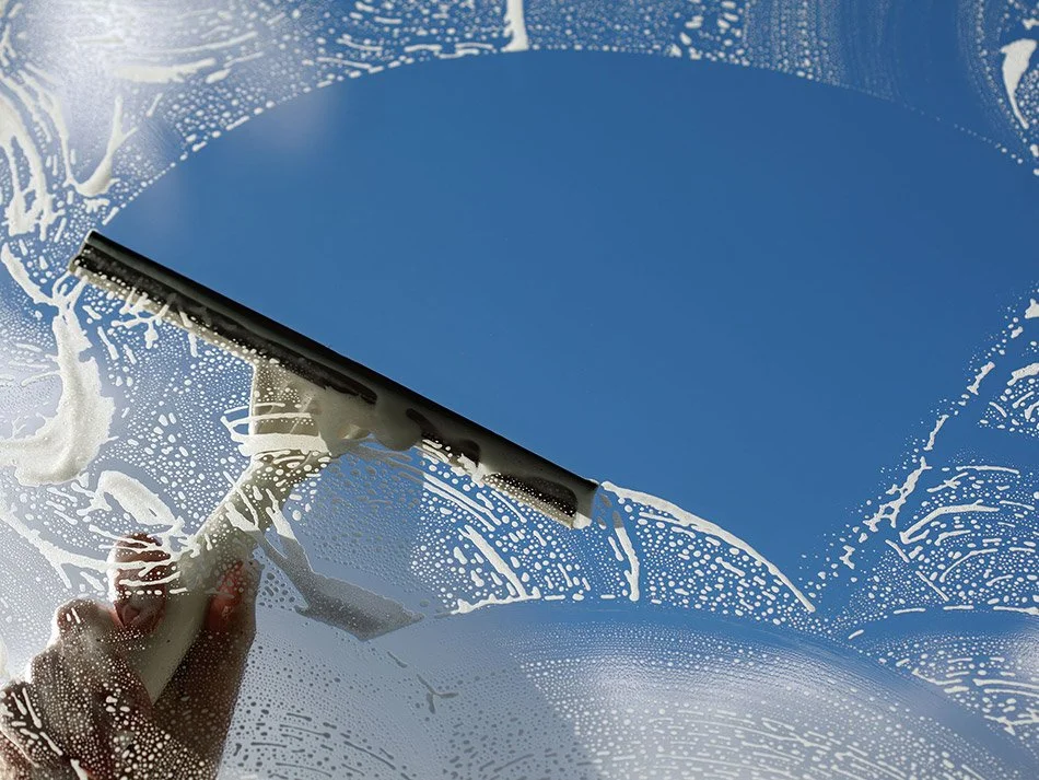 Person cleaning a window with a squeegee, creating soap suds and streaks.