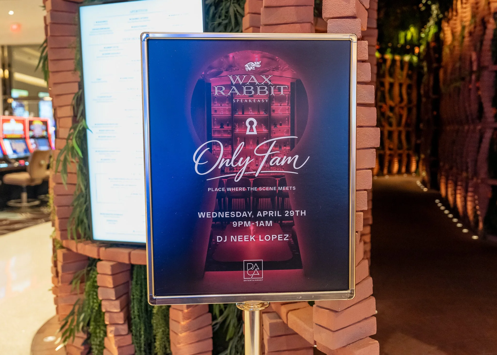 Event promotional poster for a performance called 'Wax Rabbit,' featuring a pink-hued scene of shelves with vintage items, and details about the event date, time, and DJ, displayed on a digital sign outside in a shopping mall.