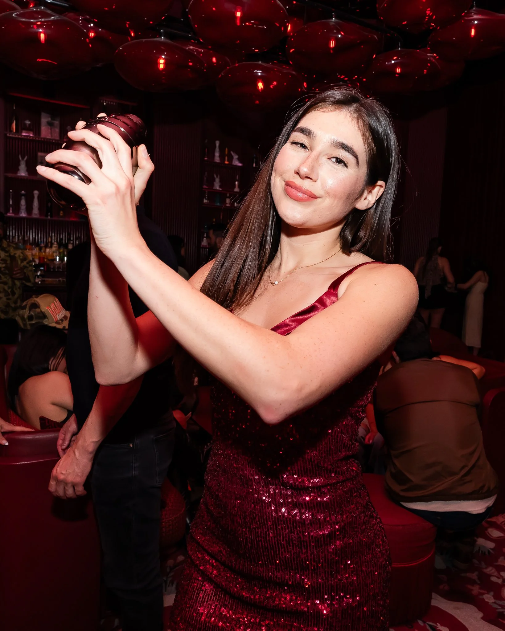 A woman in a red out fit dancing with a smile in a dimly lit with red lighting.