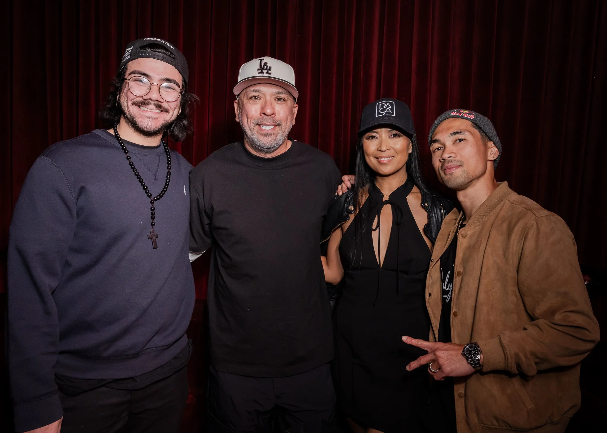 Group of four diverse people standing in front of a red curtain, smiling at the camera.