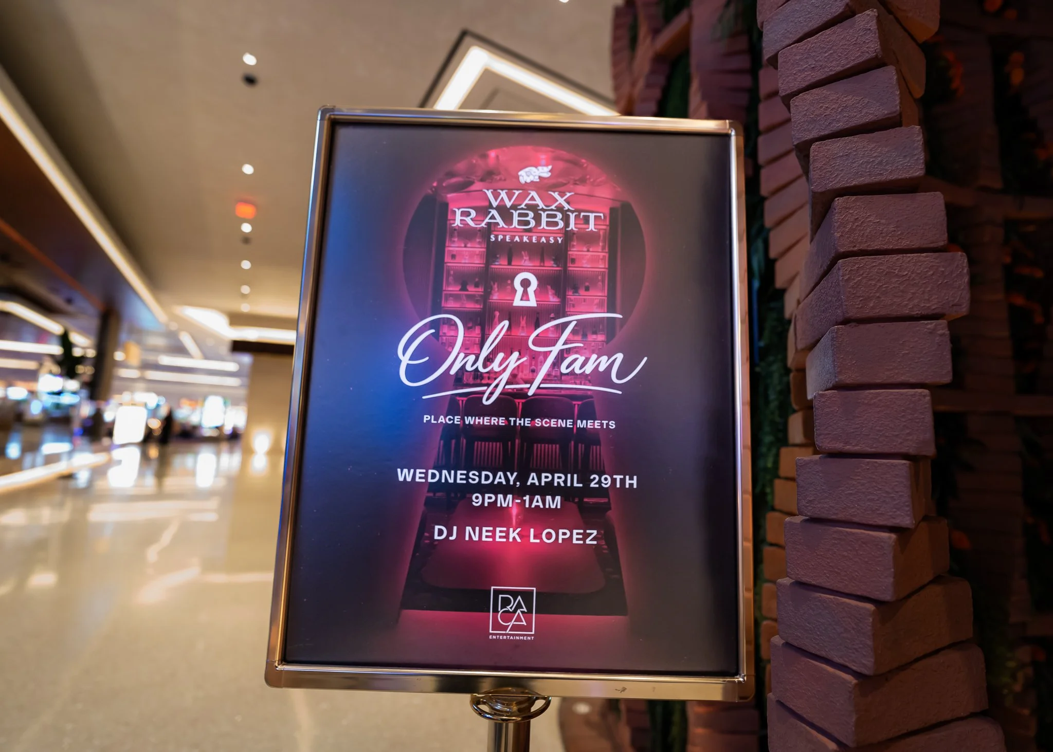 A promotional signboard for an event called 'Wax Rabbit Speakeasy' with a date of Wednesday, April 29th, from 9 PM to 1 AM, featuring DJ Neek Lopez. The sign is positioned in front of a brick wall inside a shopping mall or similar indoor venue.