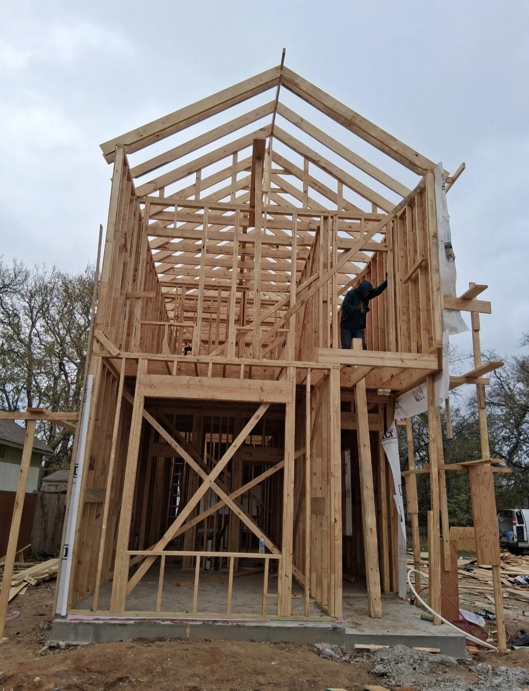 Wooden framing of a multi-story house under construction with a worker standing on the upper level.