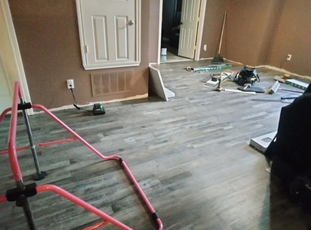 Room under renovation with tools and equipment scattered on the floor, including a pink walker, level, saw, and various construction supplies.